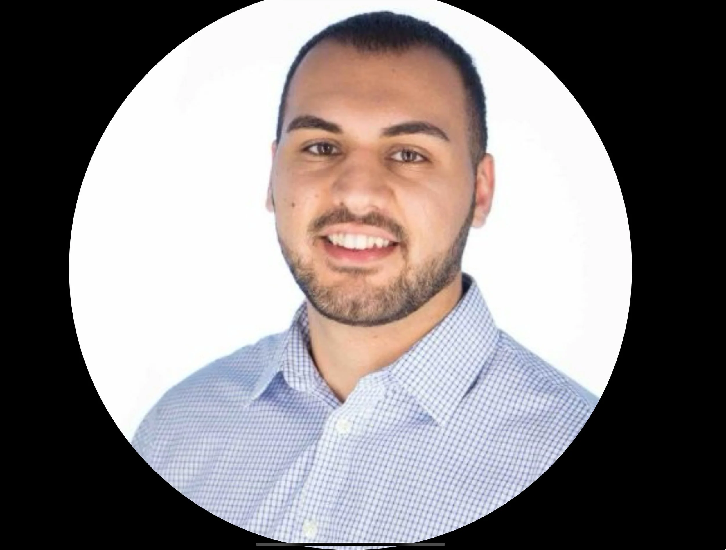 Headshot of a smiling man with short dark hair and a beard, wearing a light blue checkered shirt, against a white background.