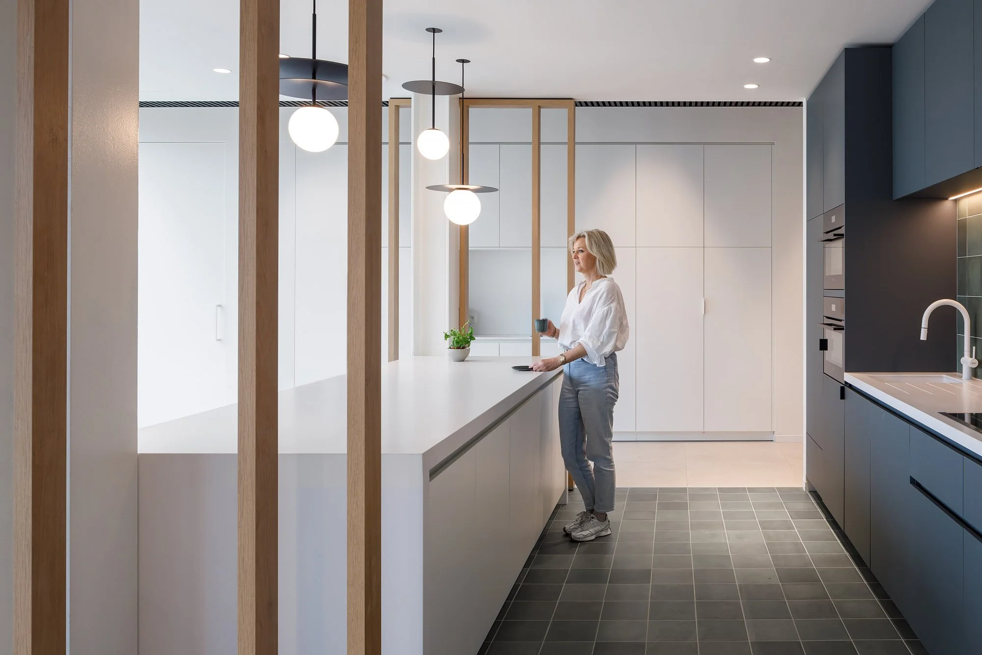 Mooie interieurarchitectuur door MAMU Architecten. Vrouw met koffie in een keuken.