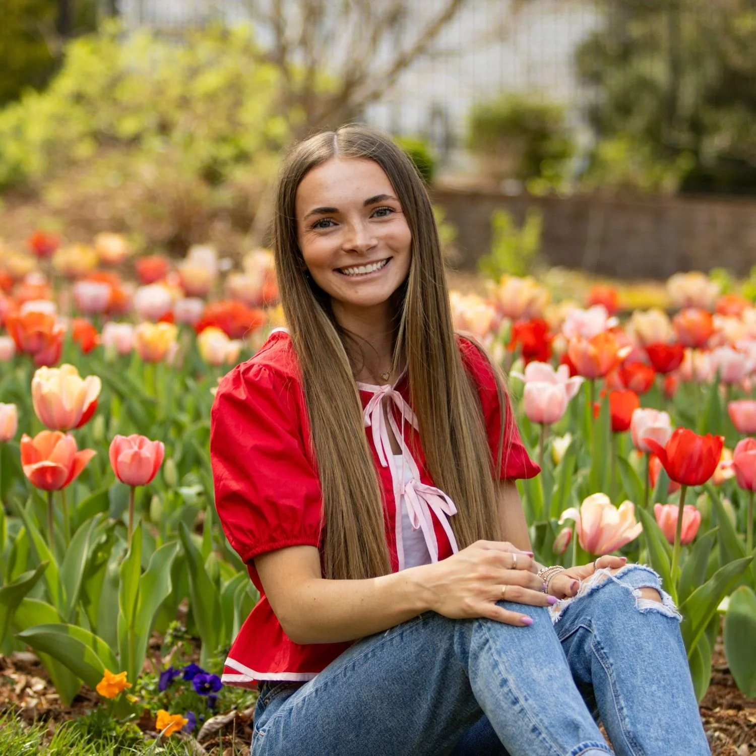 Photo of Hailey Frazier smiling in a red shirt sitting in a tulip field.