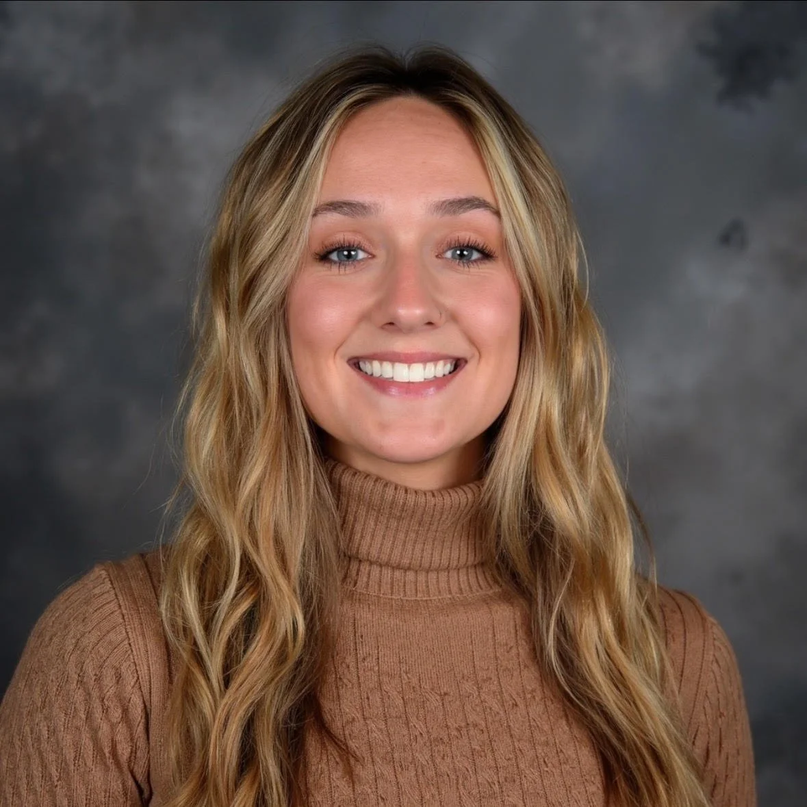 Photo of Bailey Atkins smiling in a brown turtle neck on a gray background