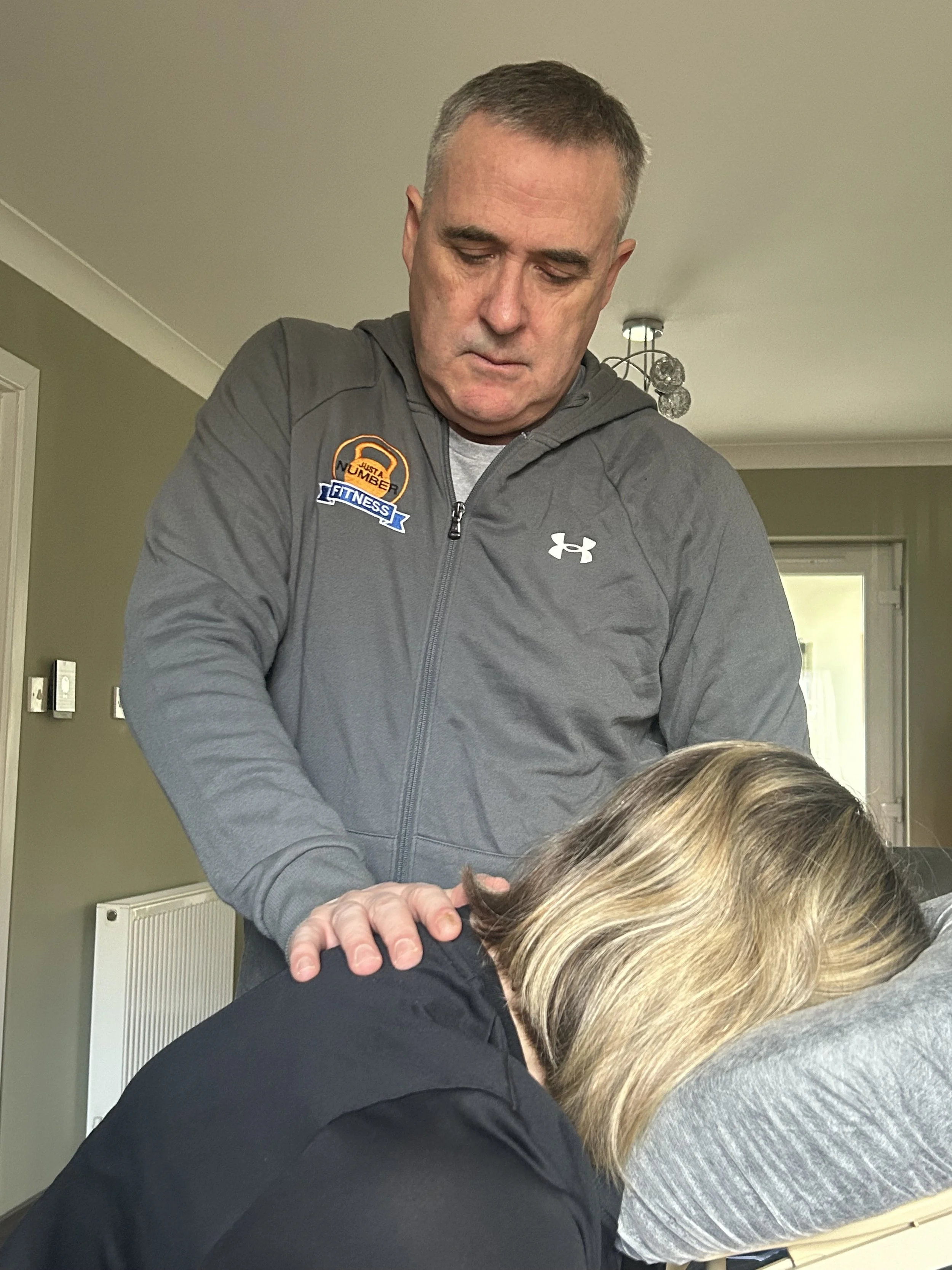 A man wearing a gray Under Armour jacket providing chiropractic care or massage therapy to a woman with blonde hair.