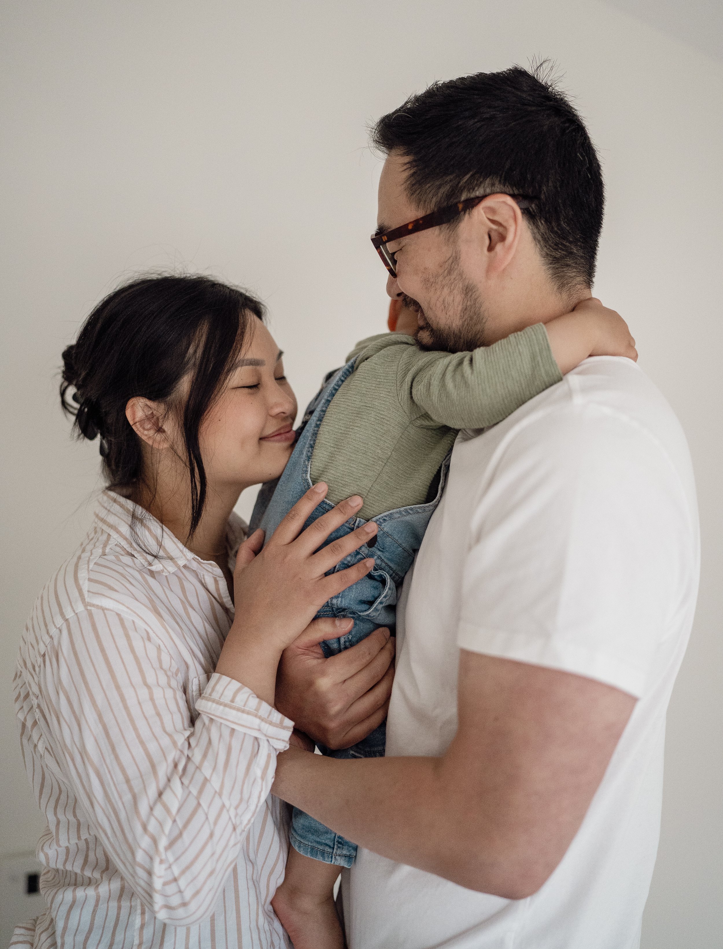 A family of three hugging and smiling, with the father holding a young child, all with happy expressions.