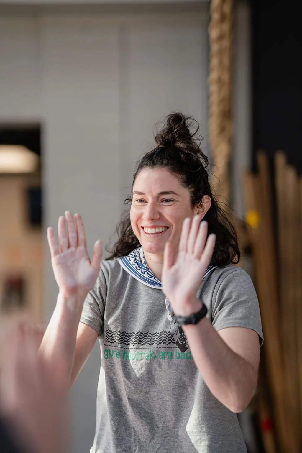 Young woman with curly hair in a bun smiling and giving her teammate a high five at an athletic event.