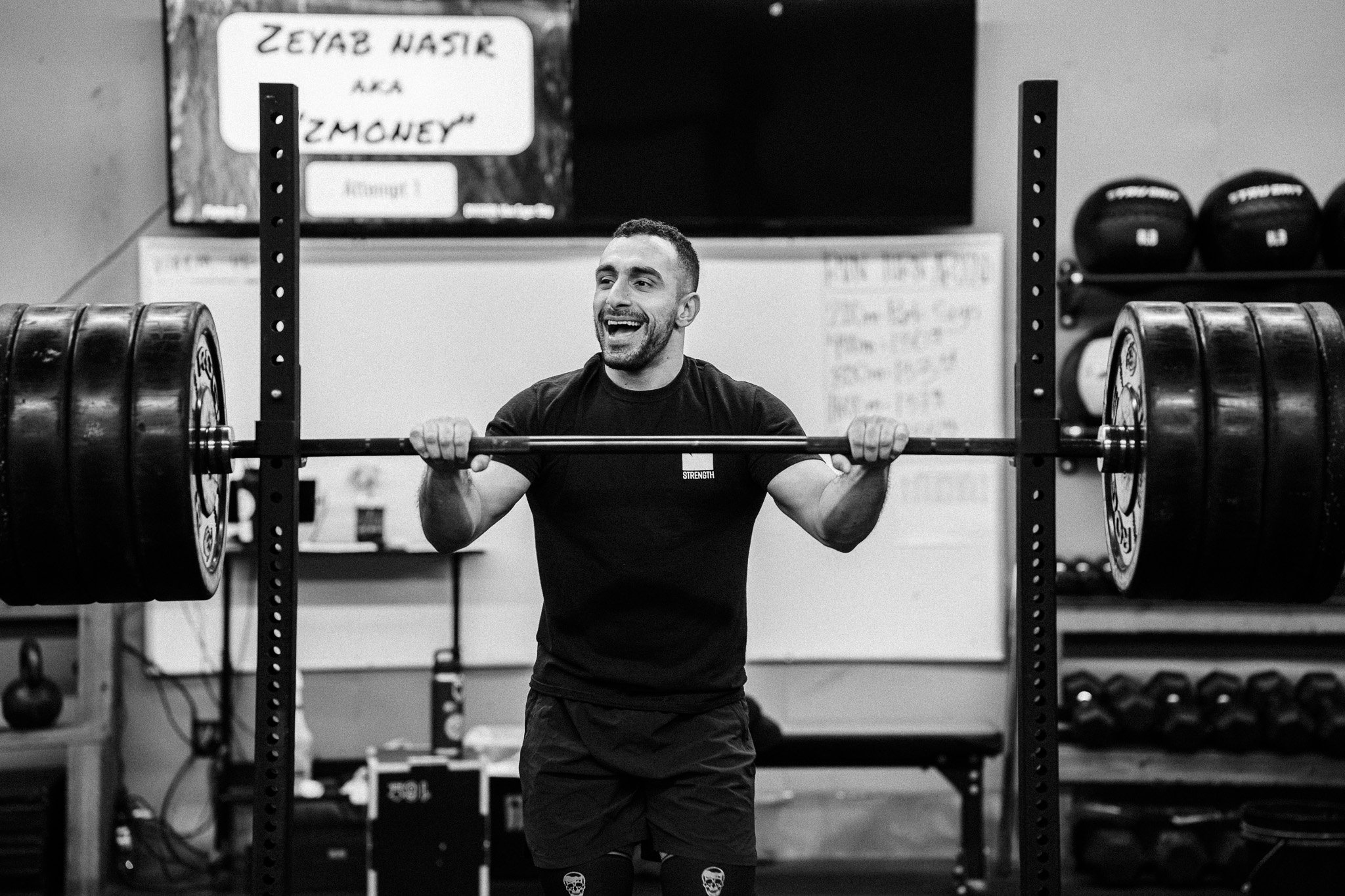 A man smiling while lifting a barbell with multiple weights at a gym.
