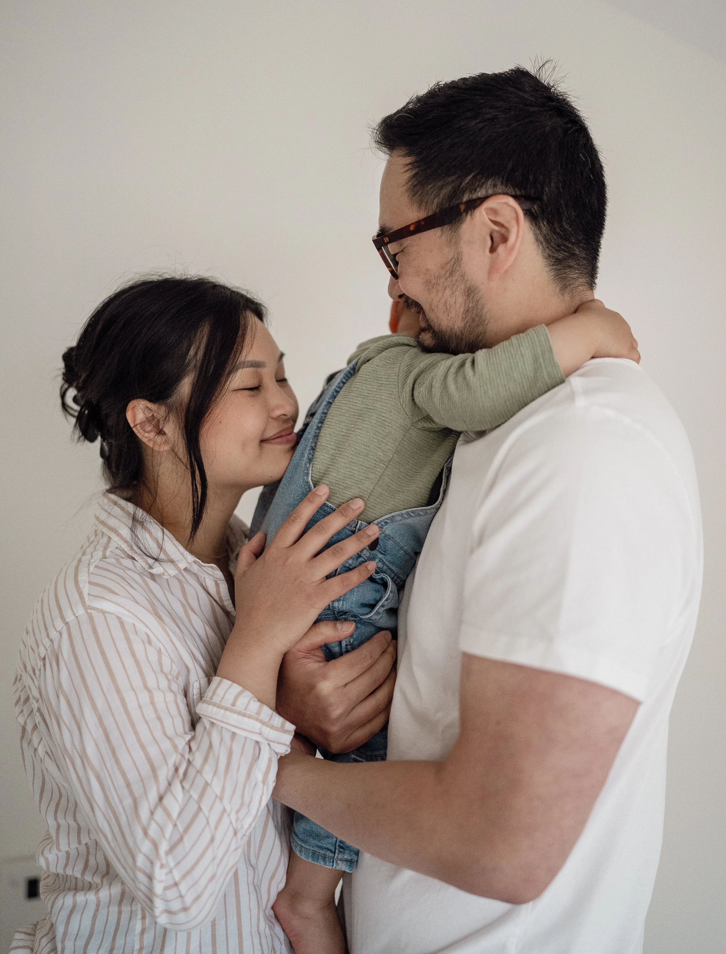 A family of three with a mother, father, and young child hugging each other in a close embrace.