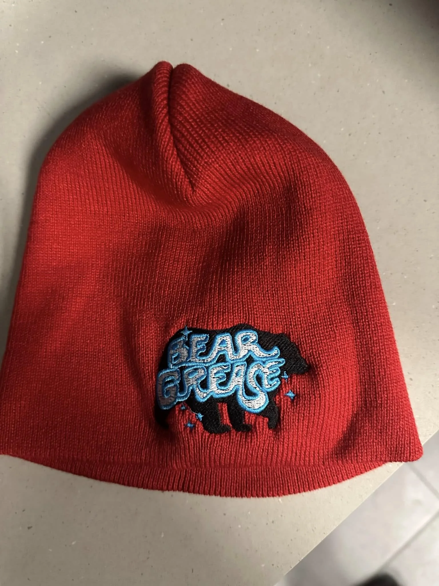 Red beanie hat with embroidered patch of a black bear and blue text reading "BEAR GREECE".