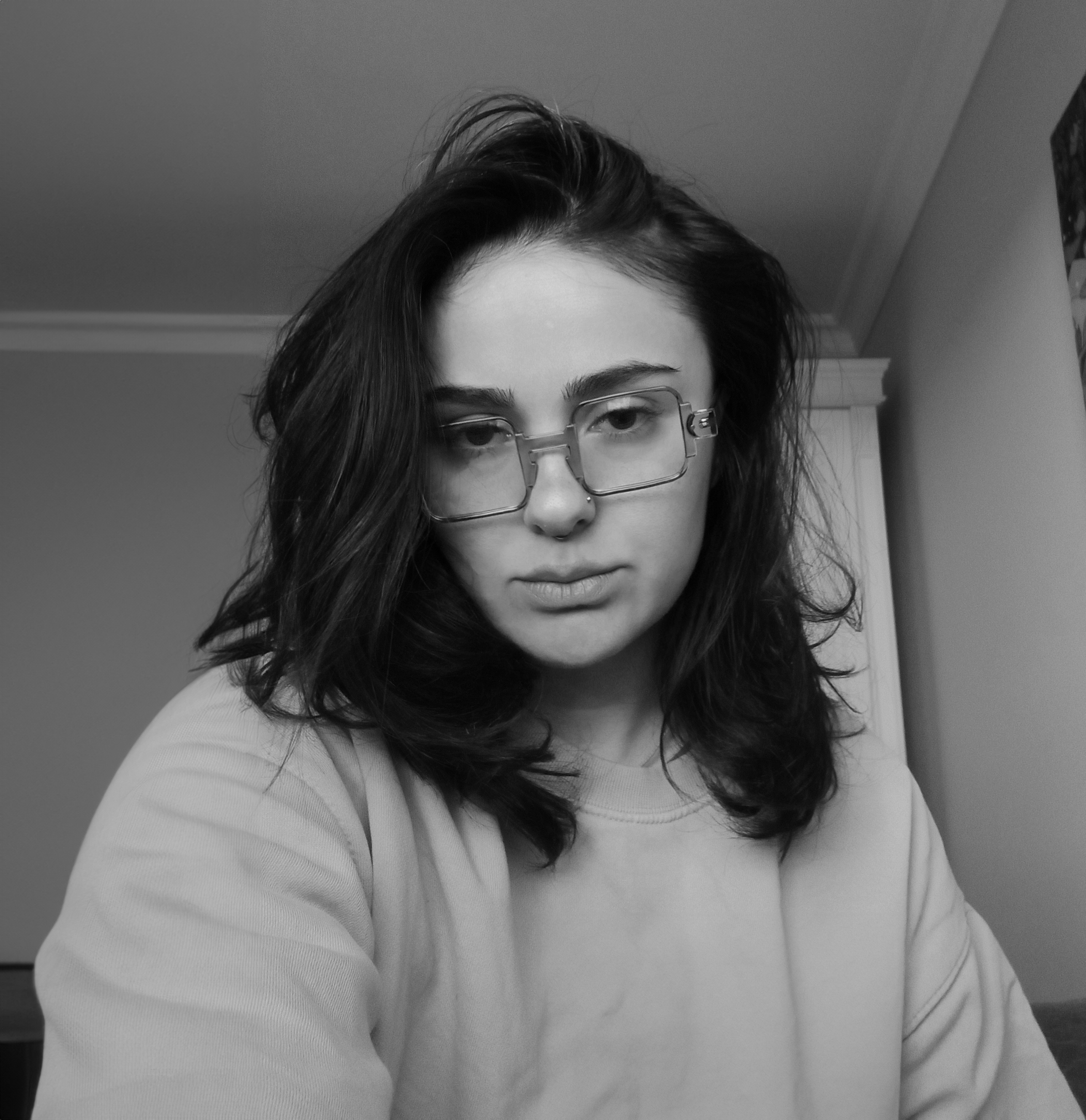 Black and white portrait of a person with long dark hair, wearing glasses and a sweatshirt, looking at the camera.