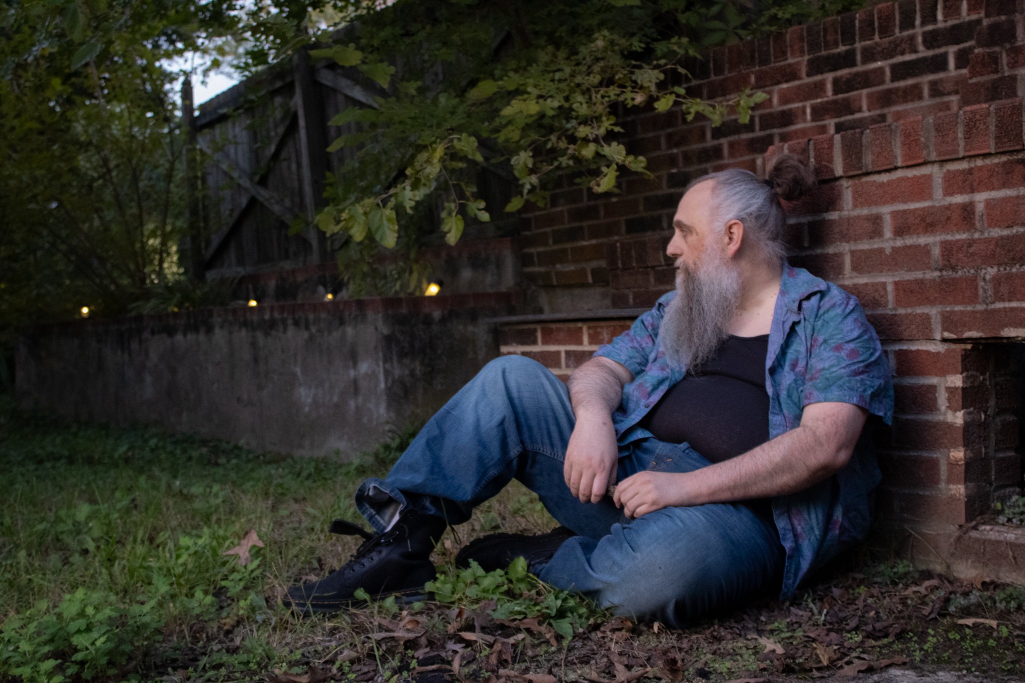 Artistic photo of a man sitting against a brick wall at twilight