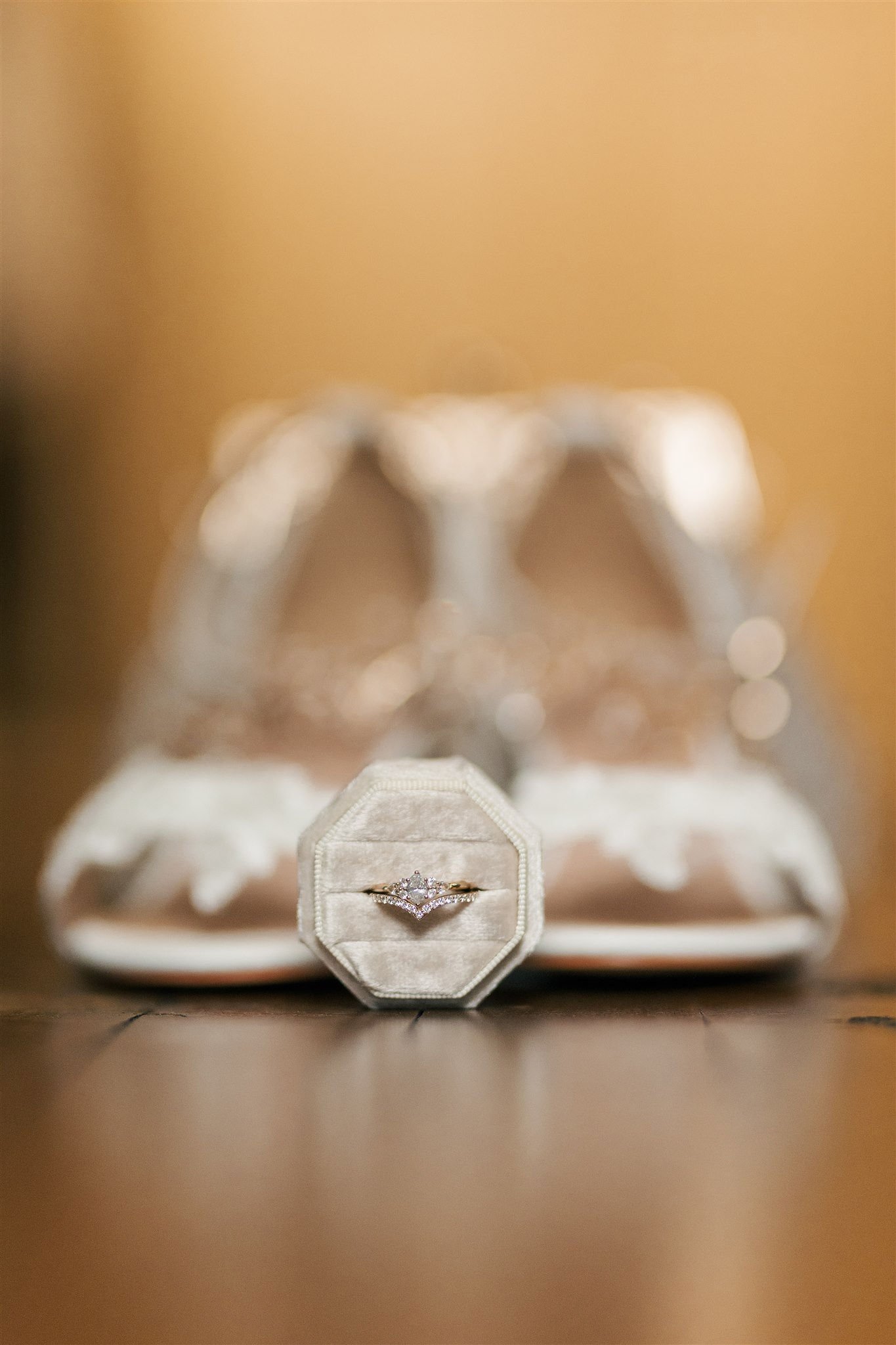 A diamond engagement ring in a velvet ring box with white sneakers in the background.
