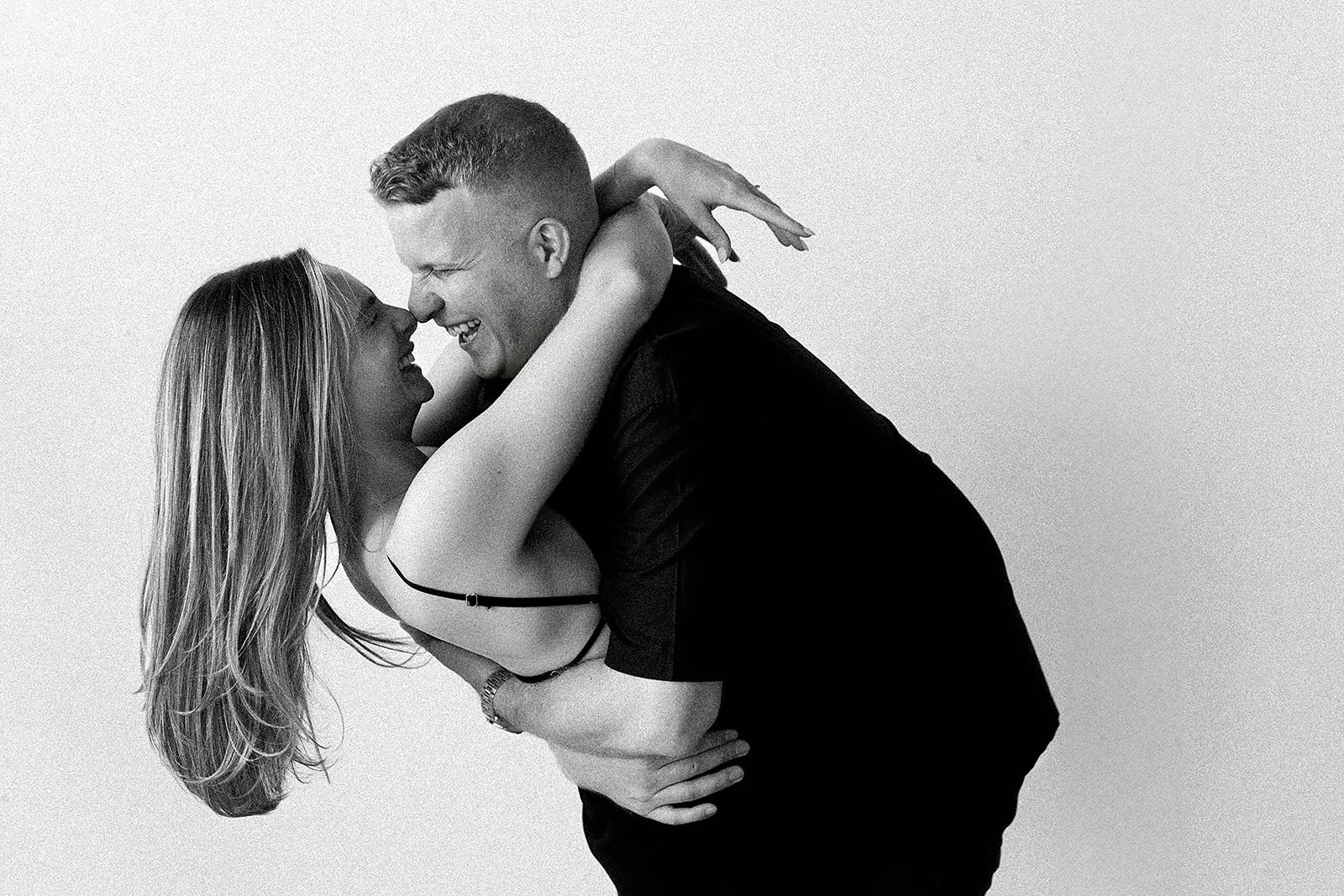 A black and white photo of a man and woman smiling and embracing each other, with the man bending forward and the woman hanging upside down.