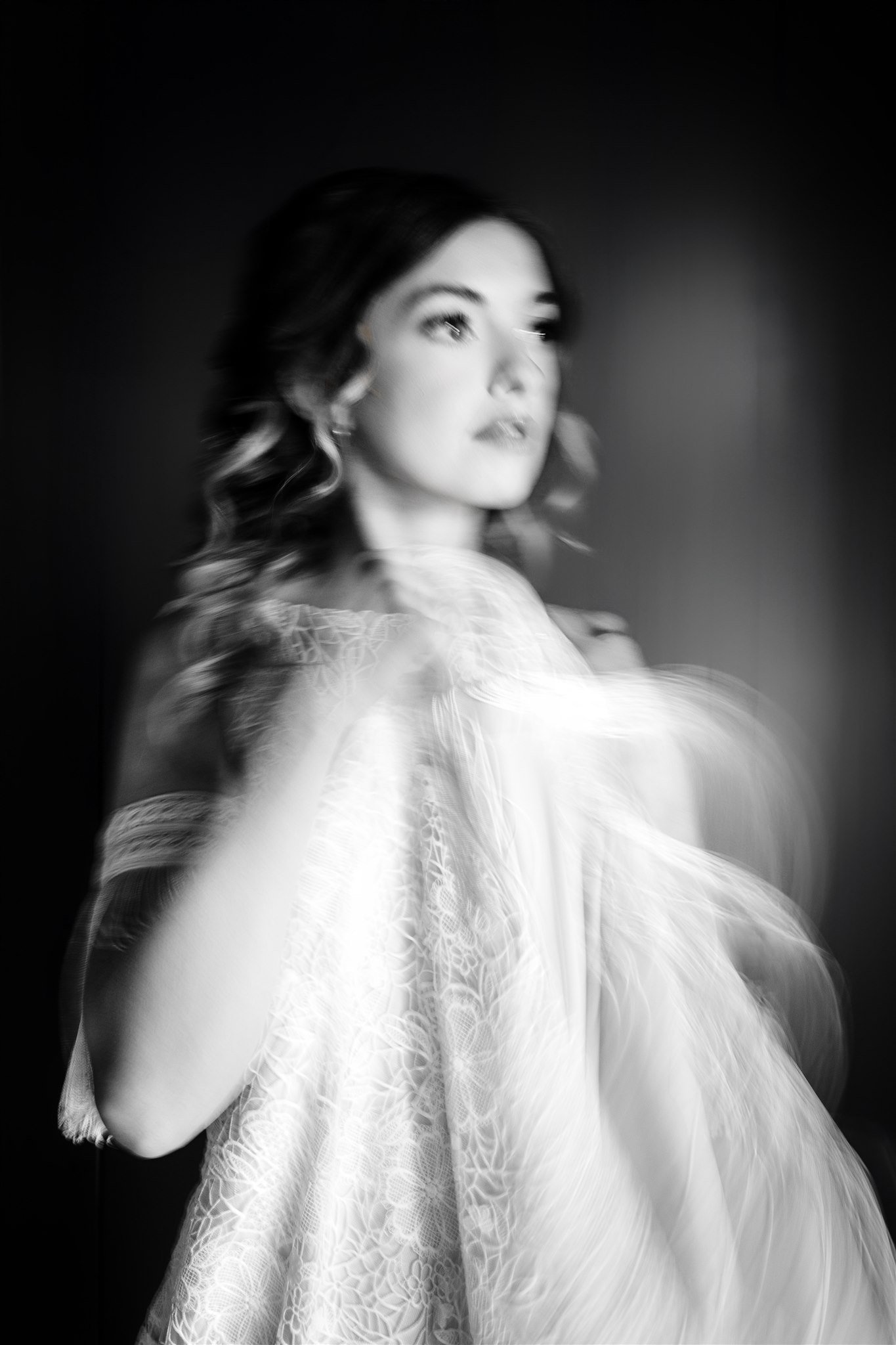 Blurred black and white portrait of a woman with wavy hair, wearing a lace dress, looking to the side.
