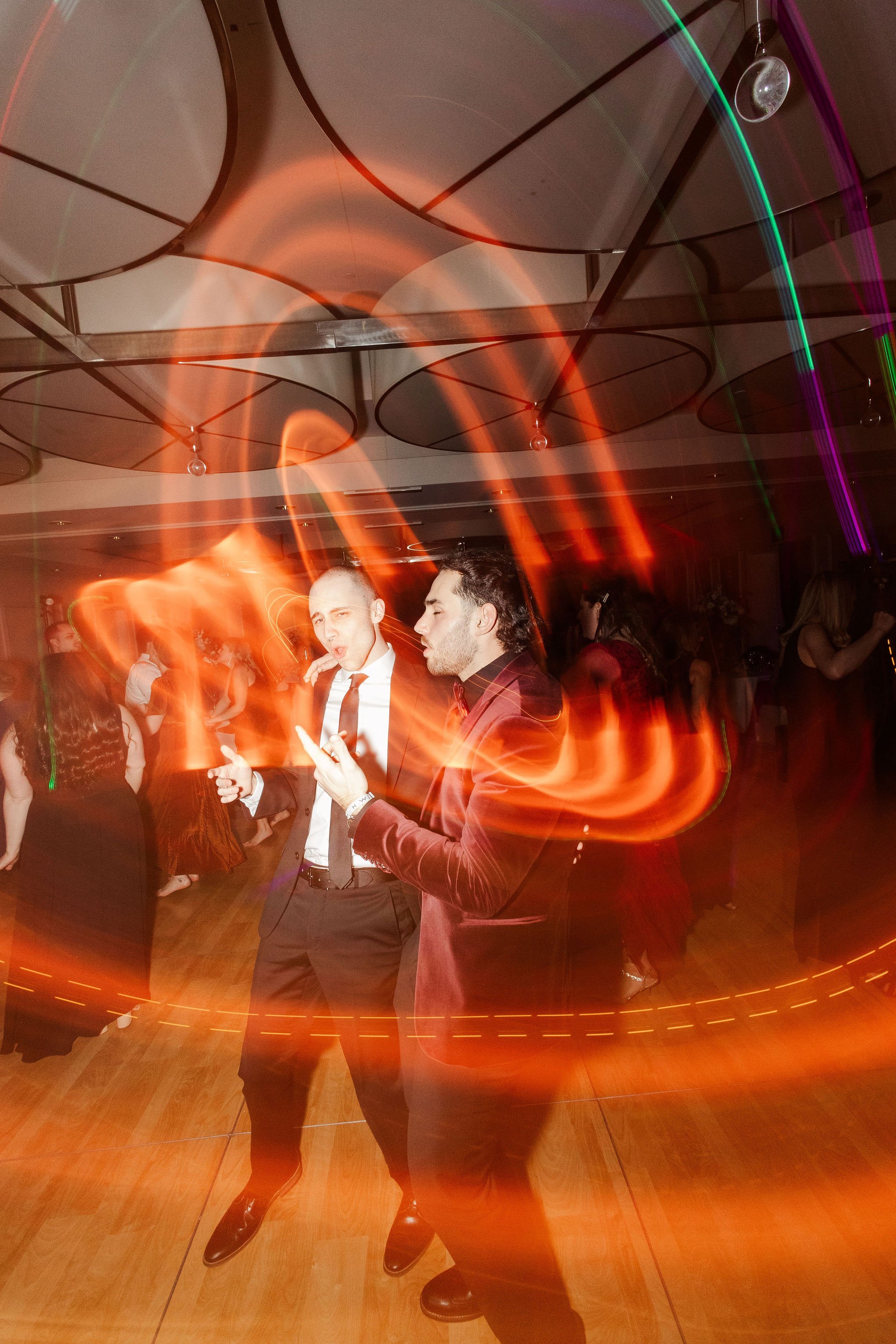 People dancing at a party with colorful lights and long-exposure effects.