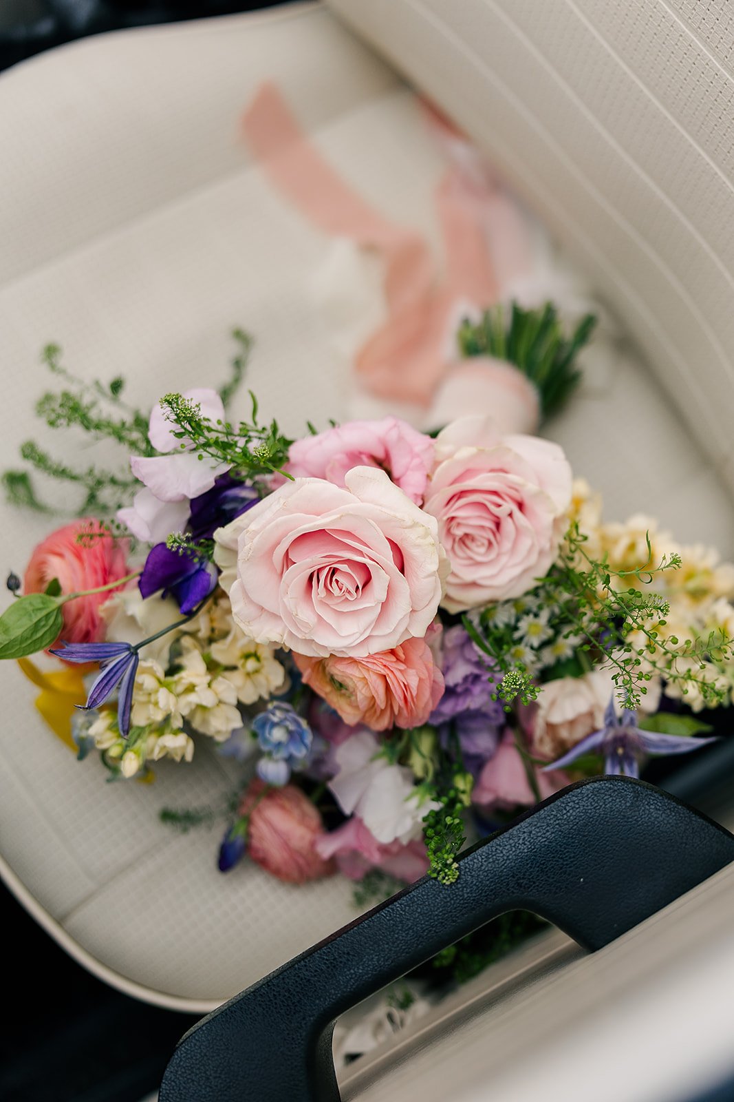 A bouquet of pink, purple, and white flowers resting on a white surface, with a navy blue handle visible in the foreground.