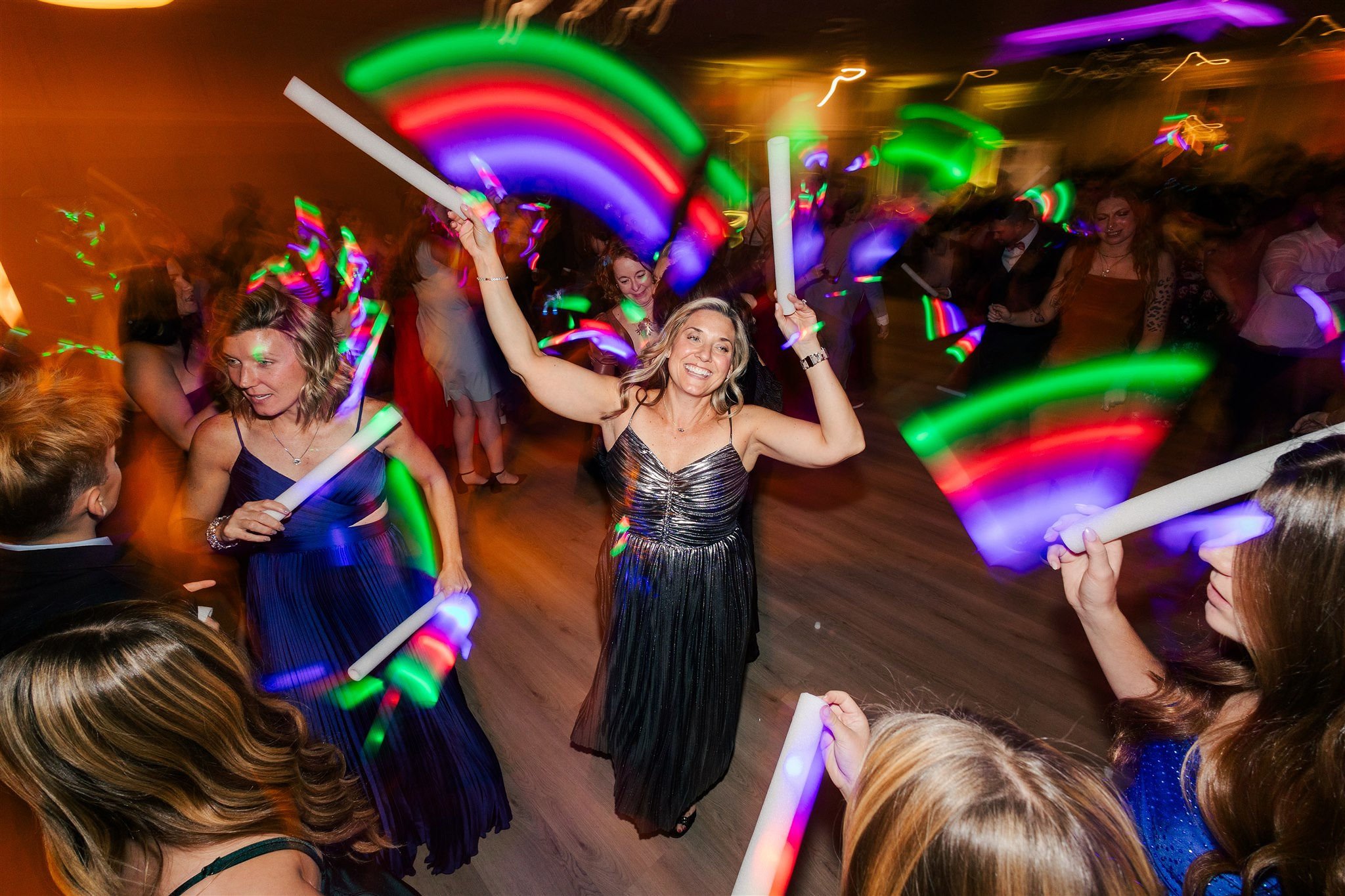 People dancing at a party with colorful glow sticks and rainbow lights, smiling and enjoying themselves.
