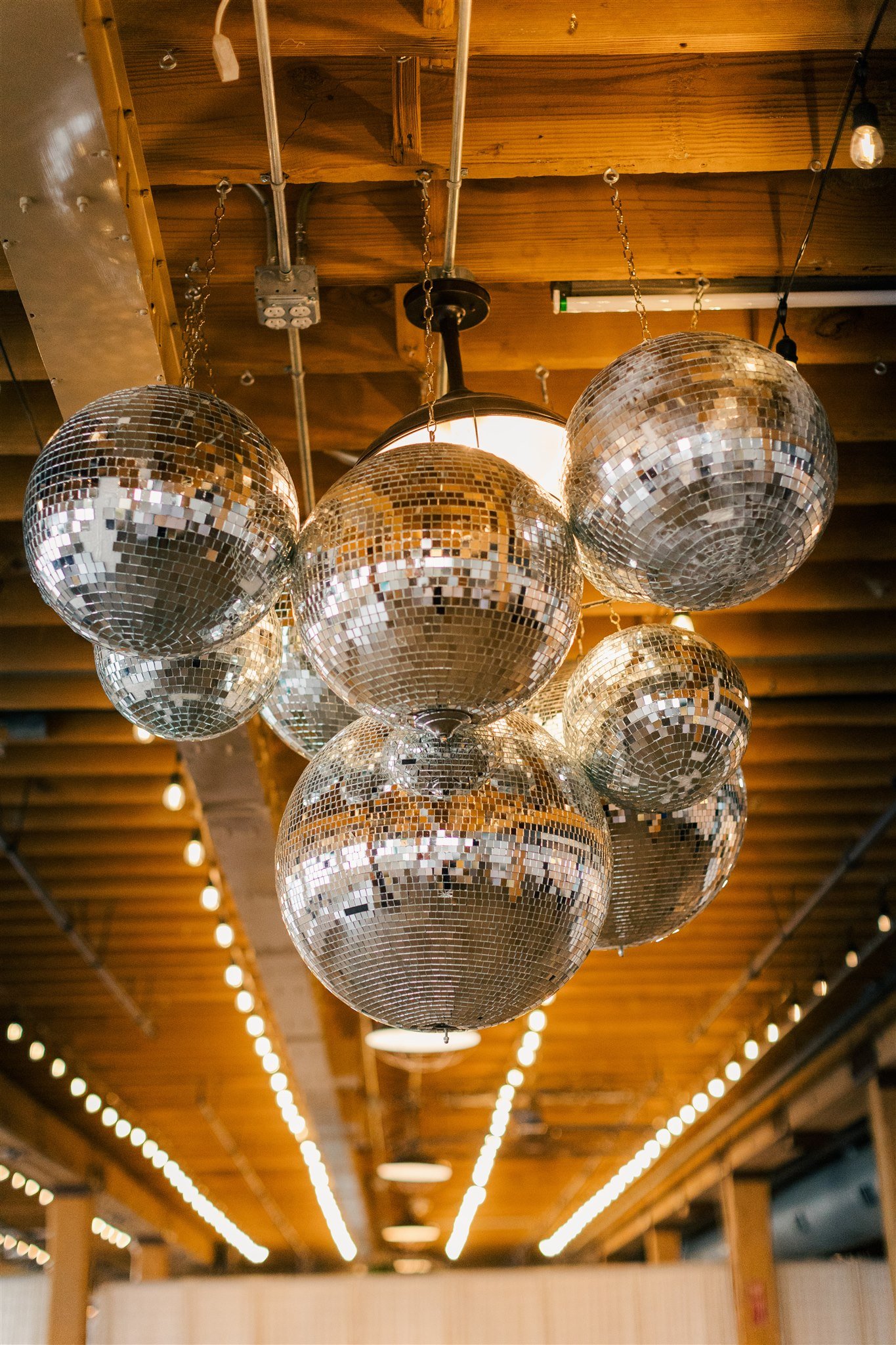 Multiple disco balls hanging from a wooden ceiling with string lights and warm lighting.