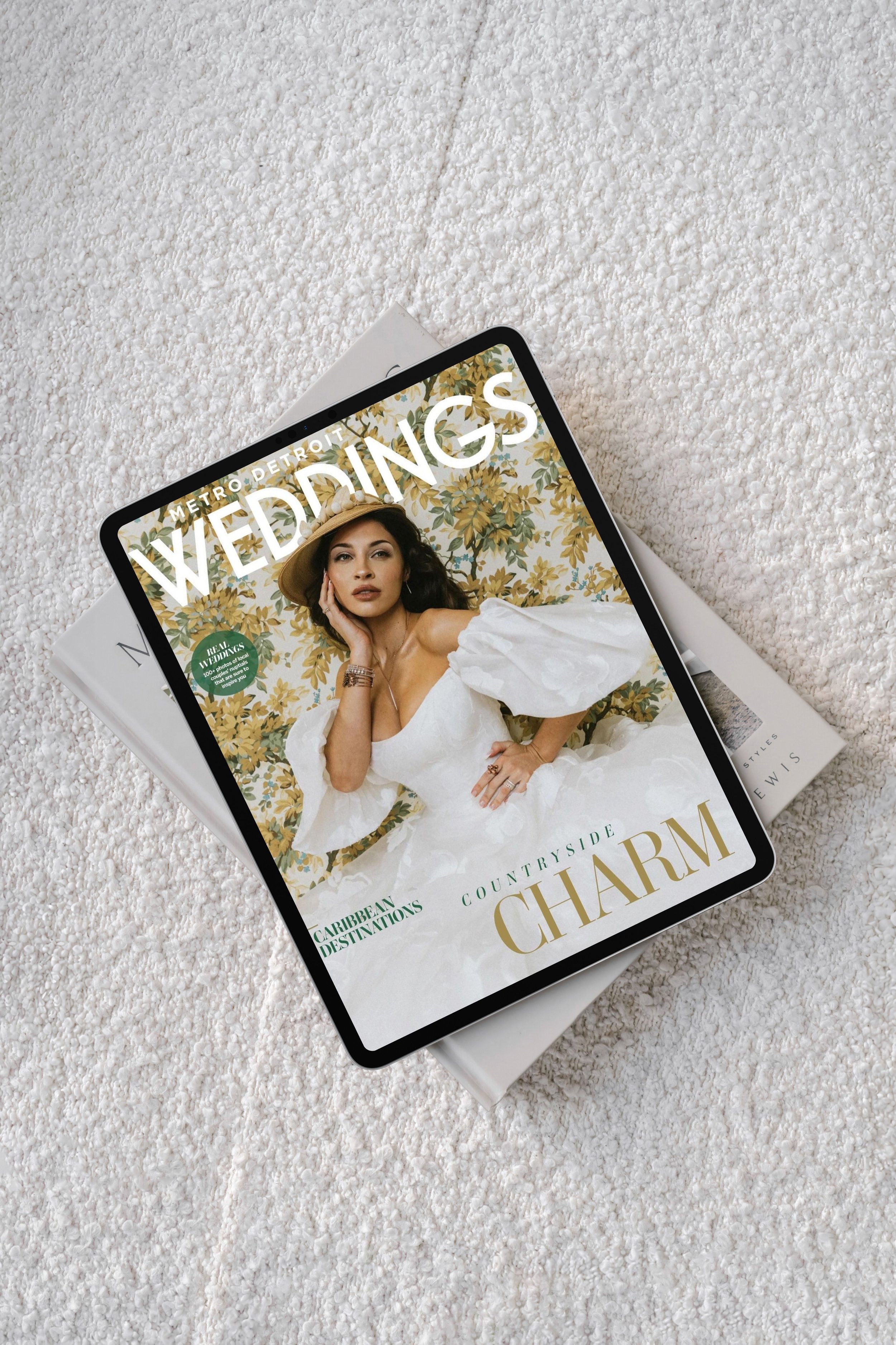 Digital magazine titled 'WEDINGS' on a tablet, featuring a woman in a white dress and wide-brimmed hat, lying on a textured white surface with a magazine underneath.