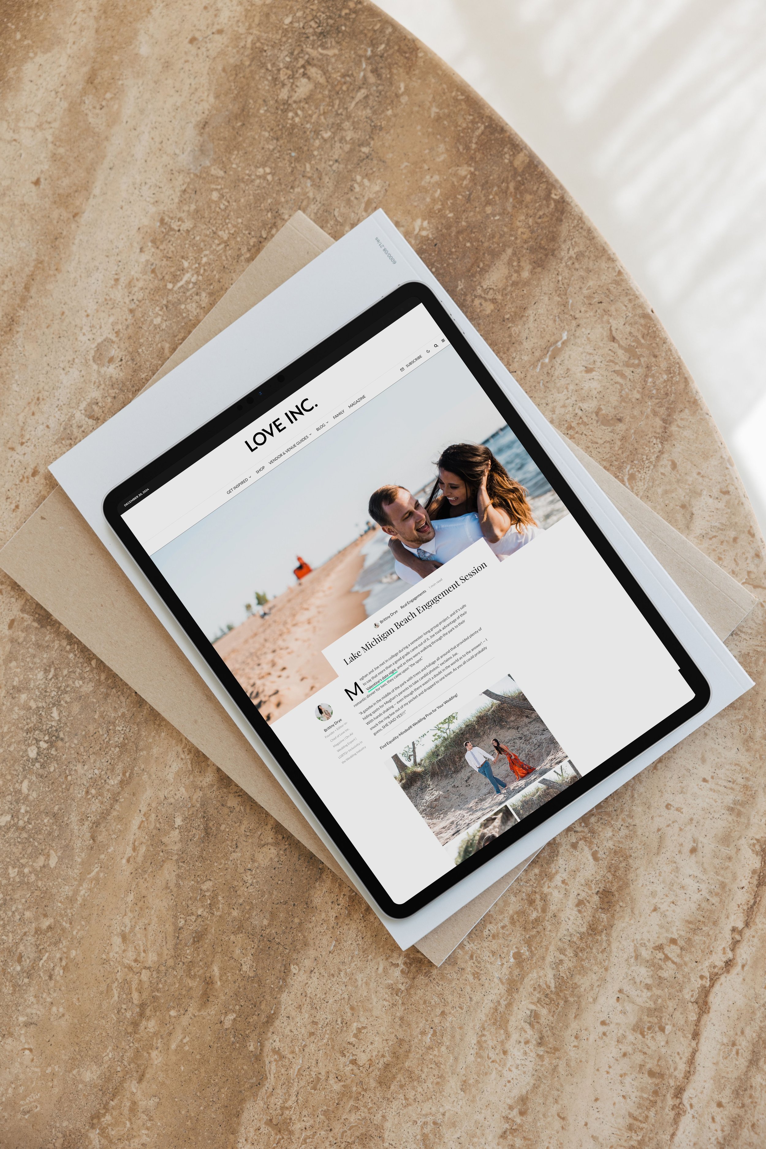 A tablet displaying a website titled 'LOVE INC.' on a beige textured surface. The webpage features a large photo of a smiling couple at the beach, with the headline 'Lake Michigan Beach Engagement Session.'