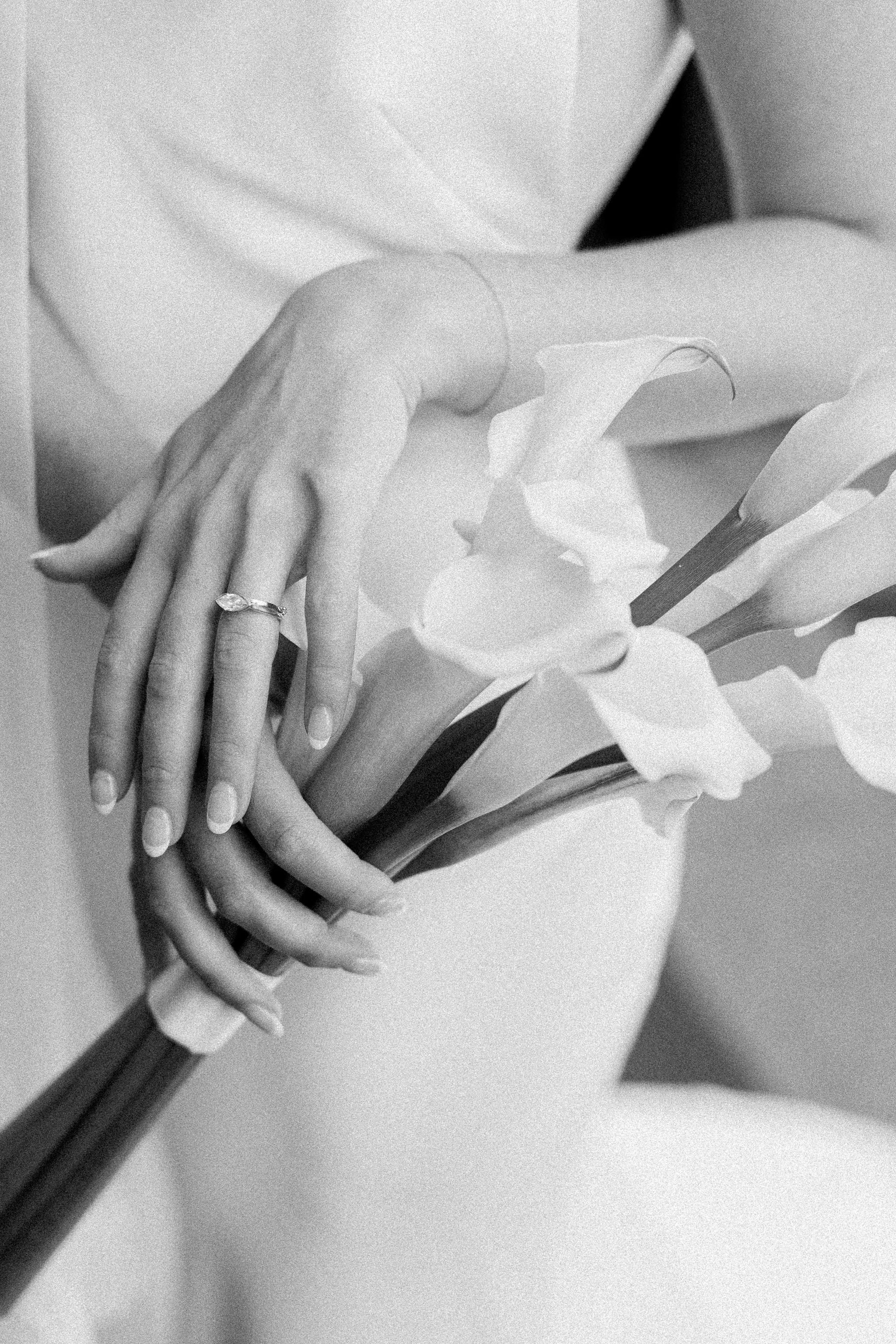 A close-up black and white photo of a person's hands holding a bouquet of flowers, with one hand wearing a ring.