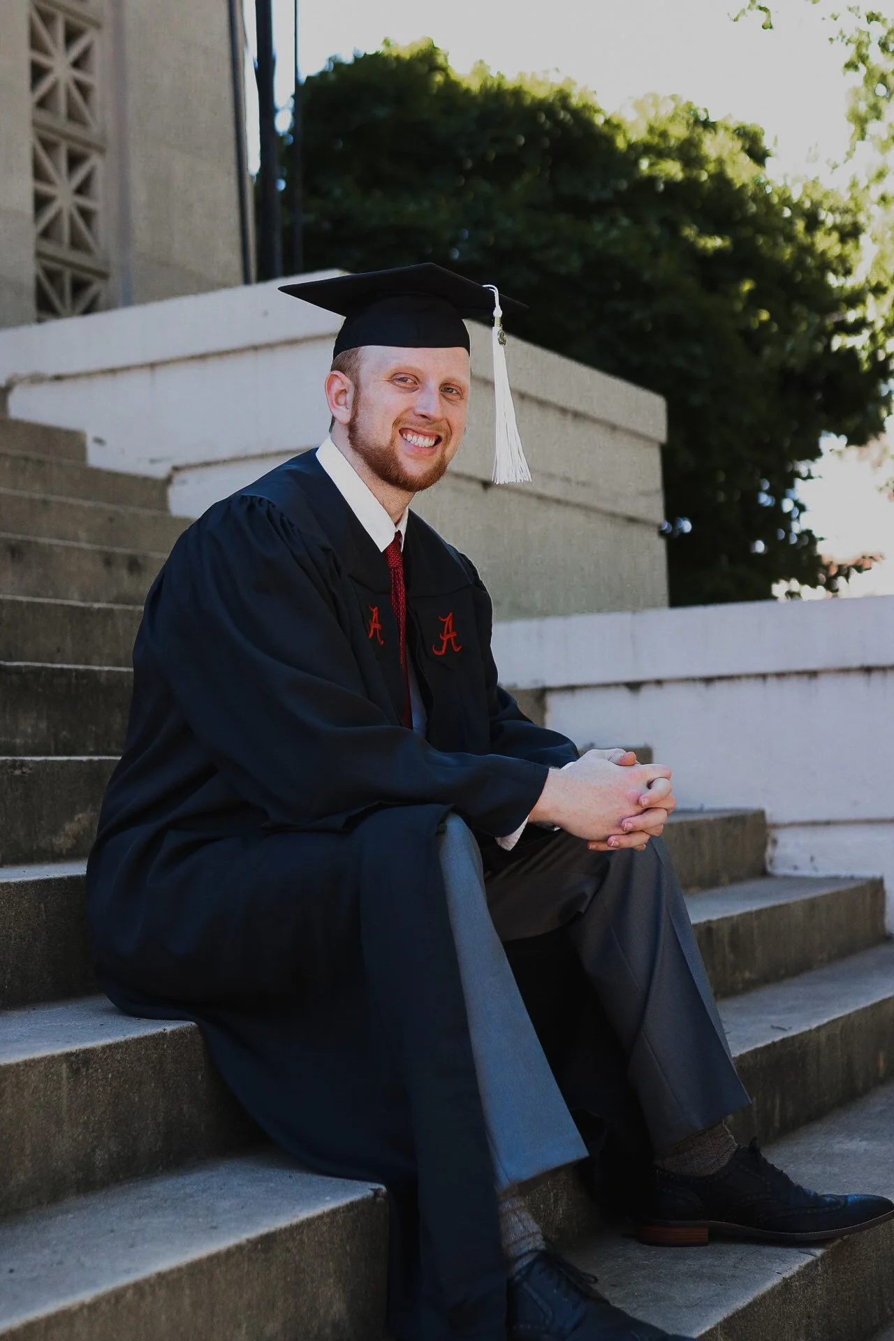 male college graduate sitting on steps in cap and gown