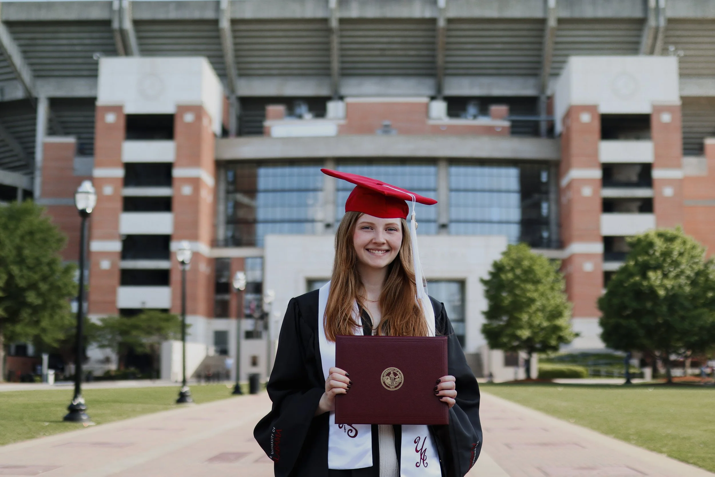 female college graduate standing outside football stadium holding degree