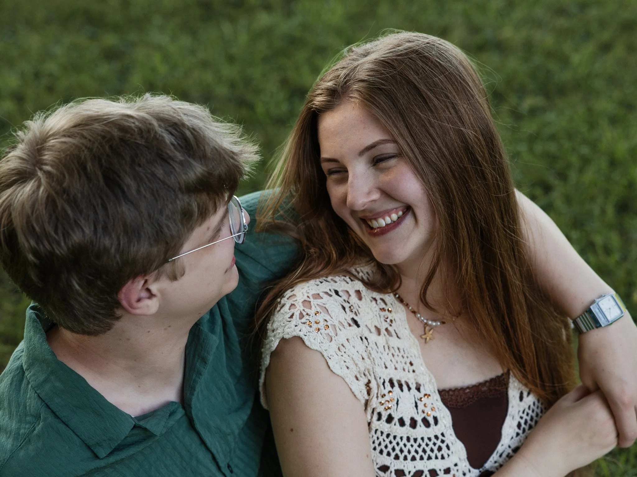 Couple smiling at each other at outdoor photography session on the grass in up close portrait.