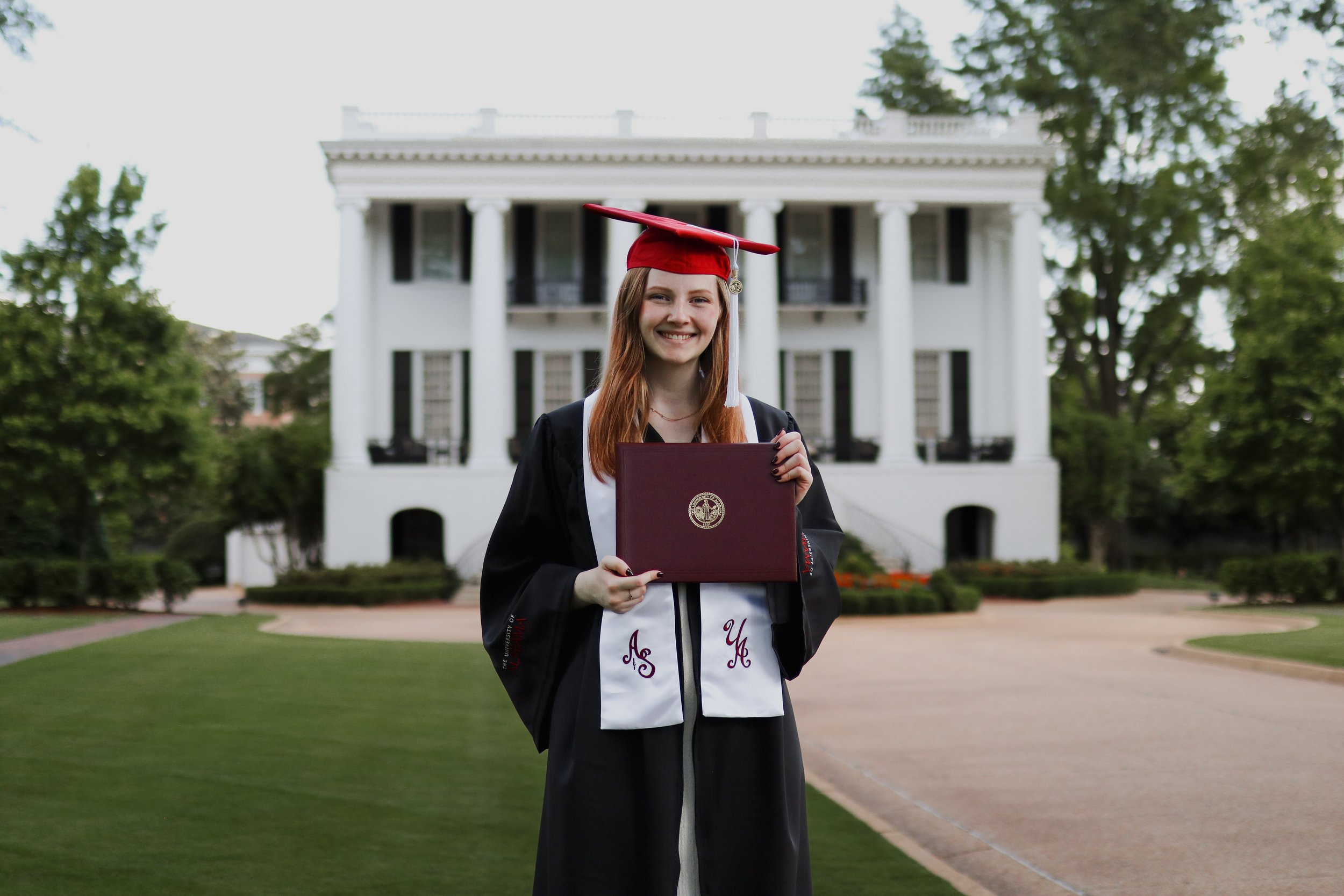 Female college graduate standing outside in cap and gown holding degree