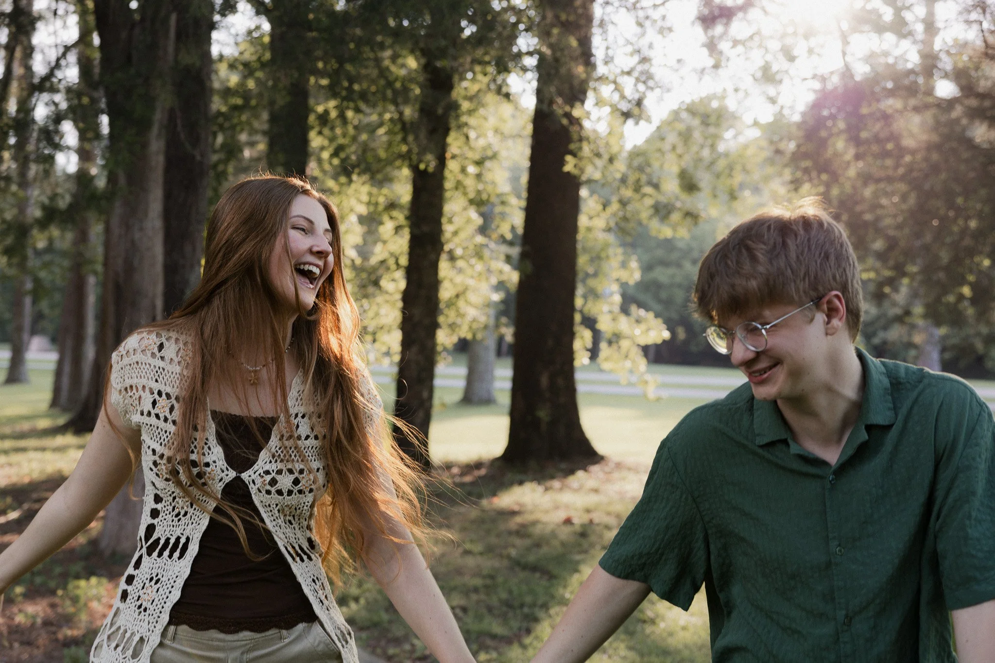 Couple laughing together while holding hands during an outdoor couples photography session in a tree-filled park.