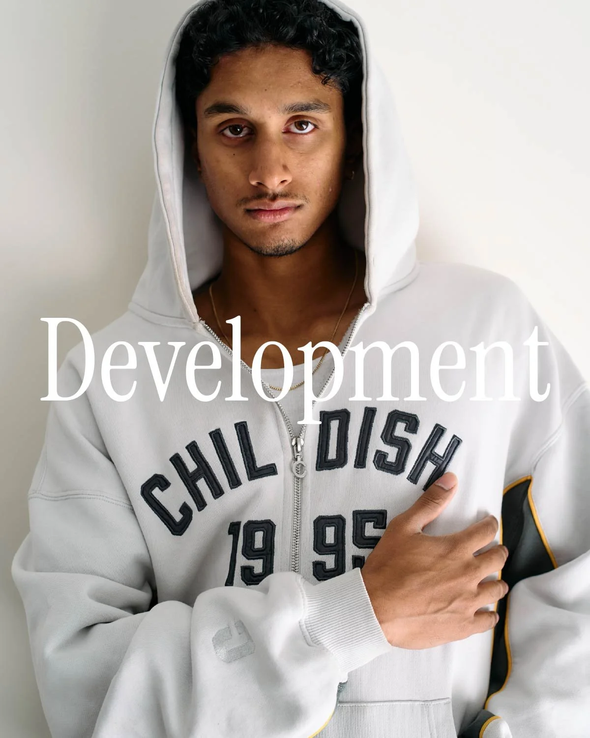A young man with dark hair wearing a white hoodie with black and yellow accents. The hoodie has the words 'Chill Dish' and the numbers '1995' on it. He stands against a plain light background. The word 'Development' is overlaid on the image.