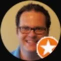 A smiling man wearing glasses with a star badge icon