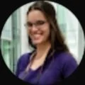 A woman with glasses and long brown hair smiling, wearing a purple blazer.