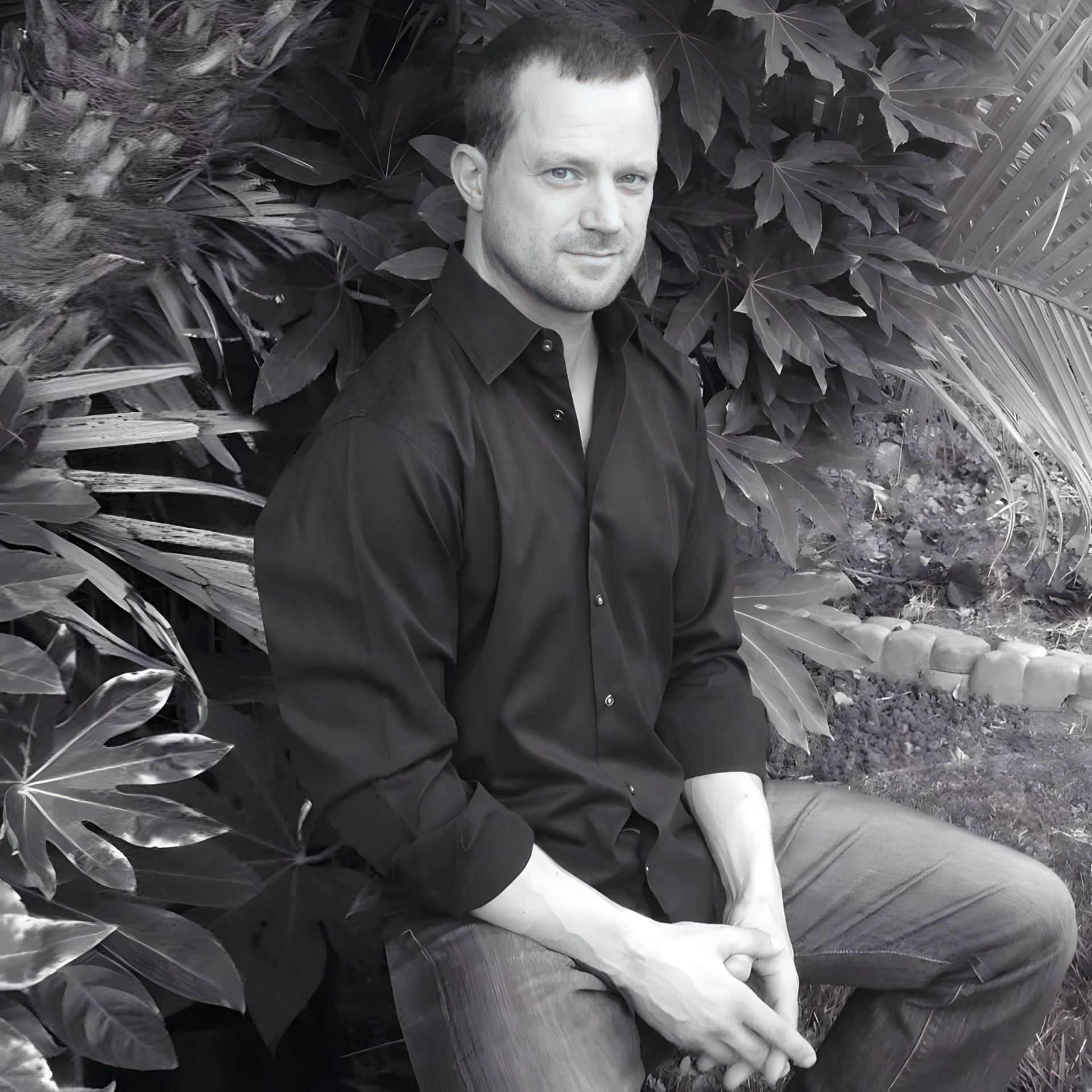 Man in black shirt sitting amidst tropical plants in black and white