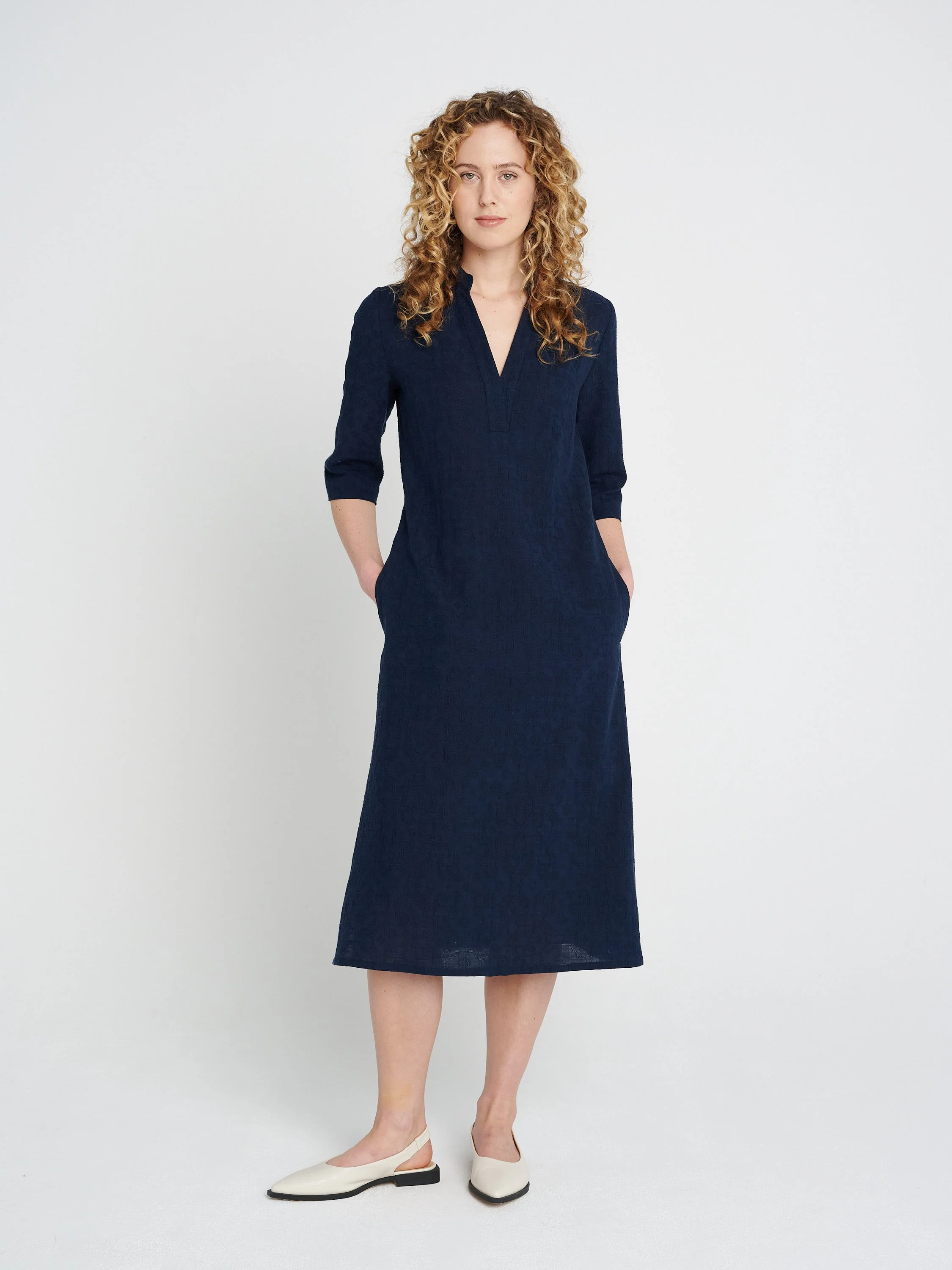 Lässiges, gerade geschnittenes dunkelblaues Kleid mit Tunika-Ausschnitt und dreiviertel-Ärmeln, Schlitzen und Taschen.