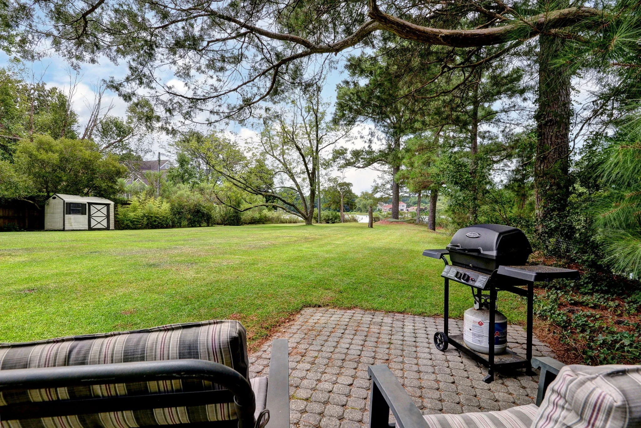 A backyard with a lawn, trees, a shed, and patio furniture with a gas grill.