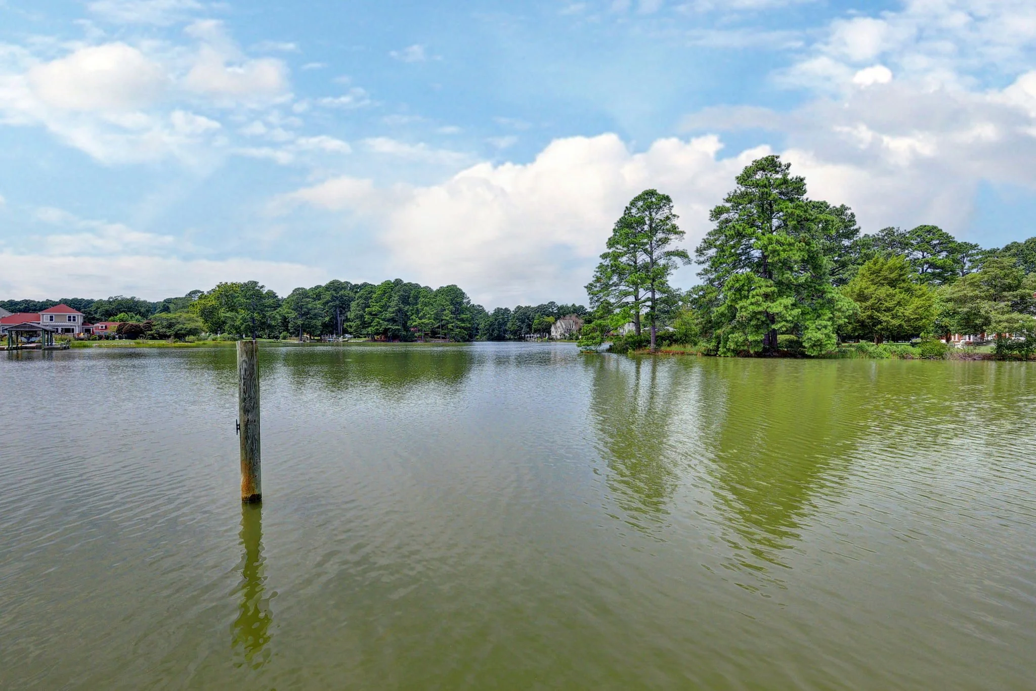 A peaceful lake with calm water, green trees on the shoreline, and a partly cloudy sky.