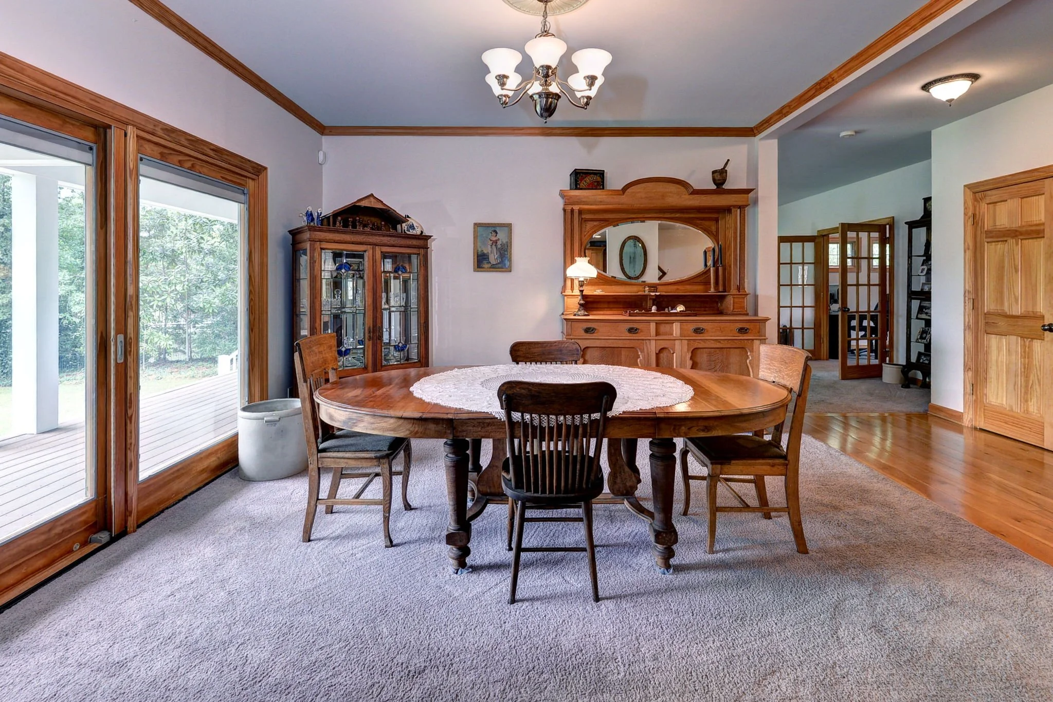 Dining room with a wooden oval table, six chairs, a china cabinet, a dresser with a mirror, and sliding glass doors leading outside.