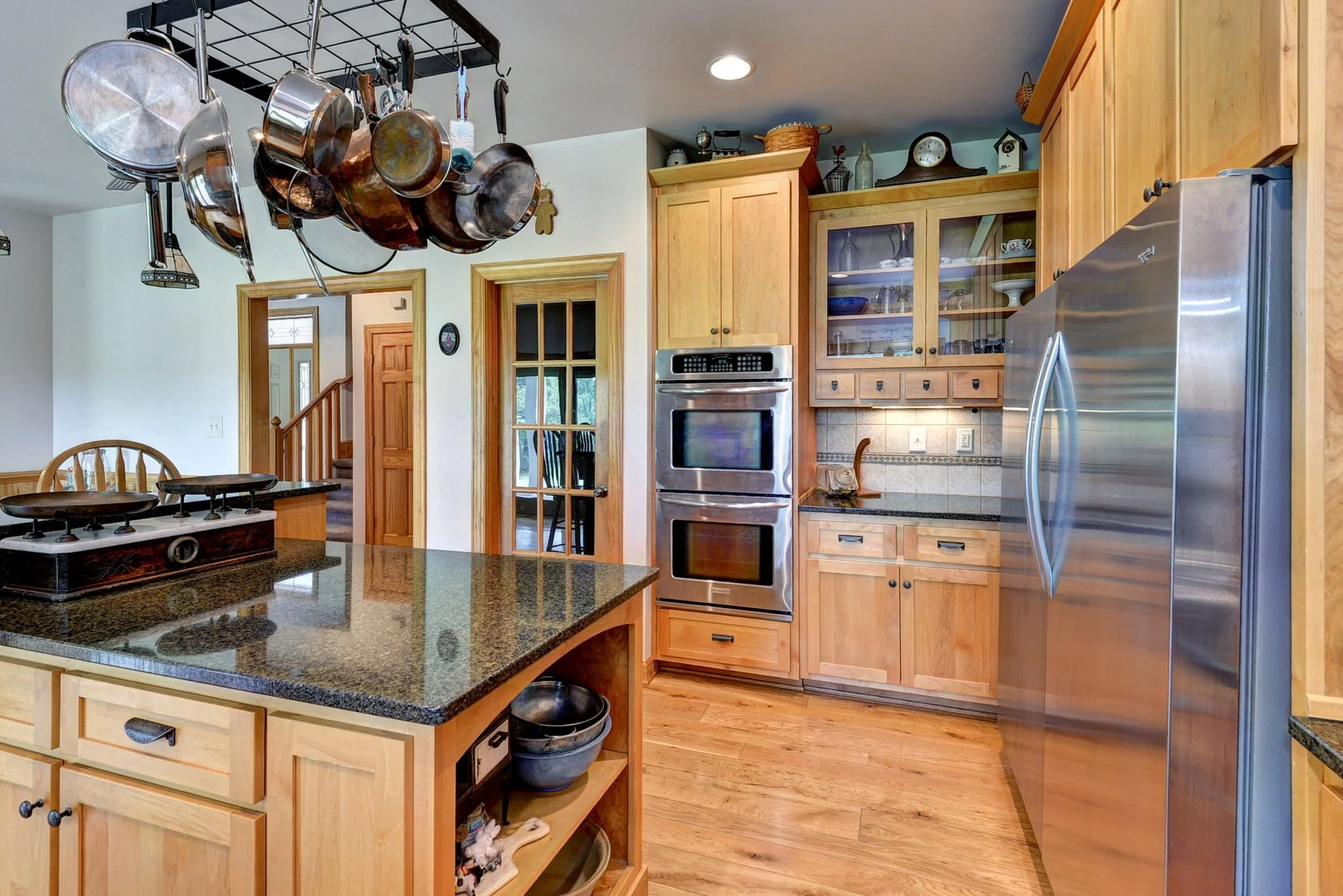 Kitchen with wooden cabinets, stainless steel appliances, hanging pots and pans, and wooden flooring.