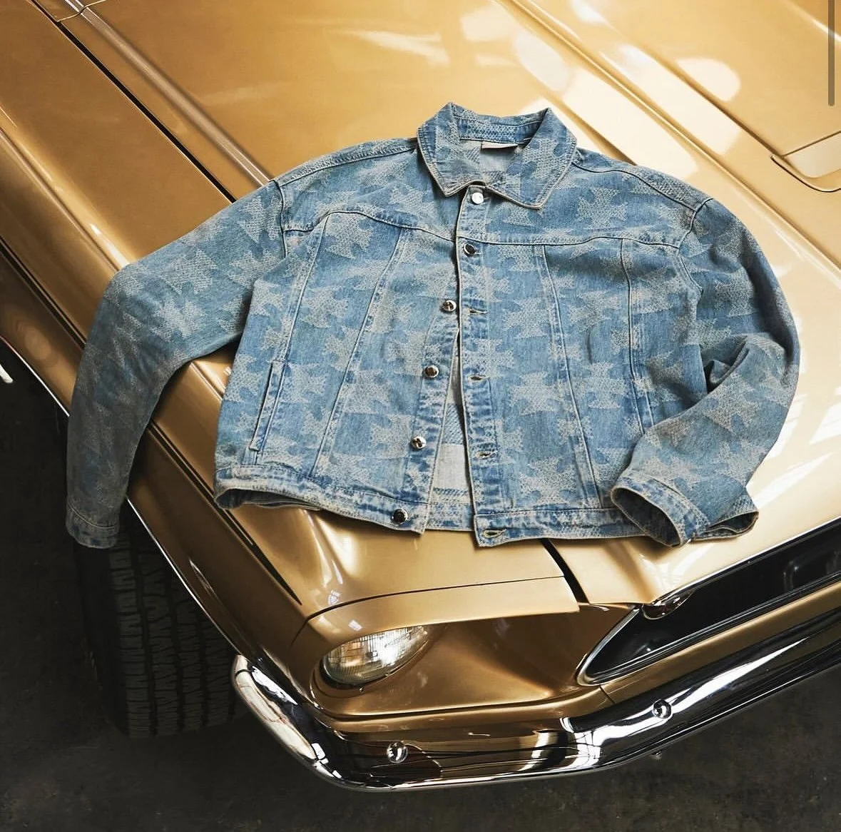 A denim jacket lying on the hood of a vintage gold car.