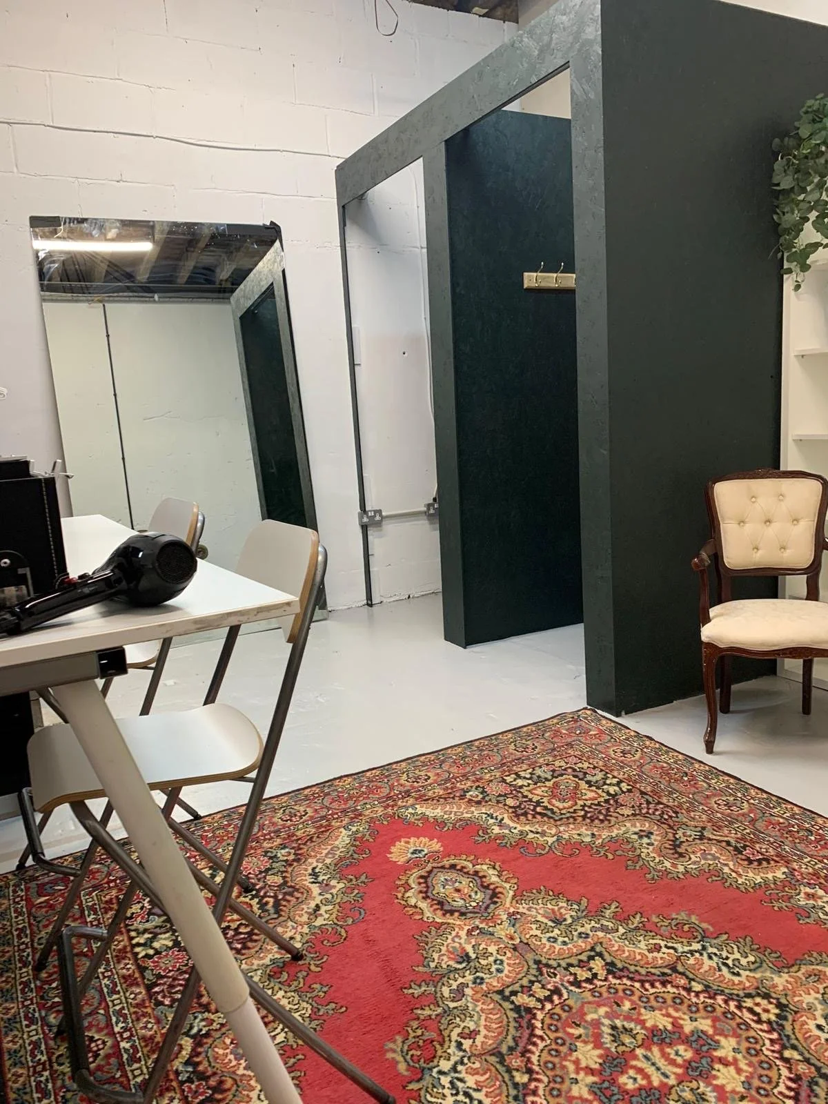 Interior room with vintage armchair, large mirror, table with hairdryer, and Persian-style rug.