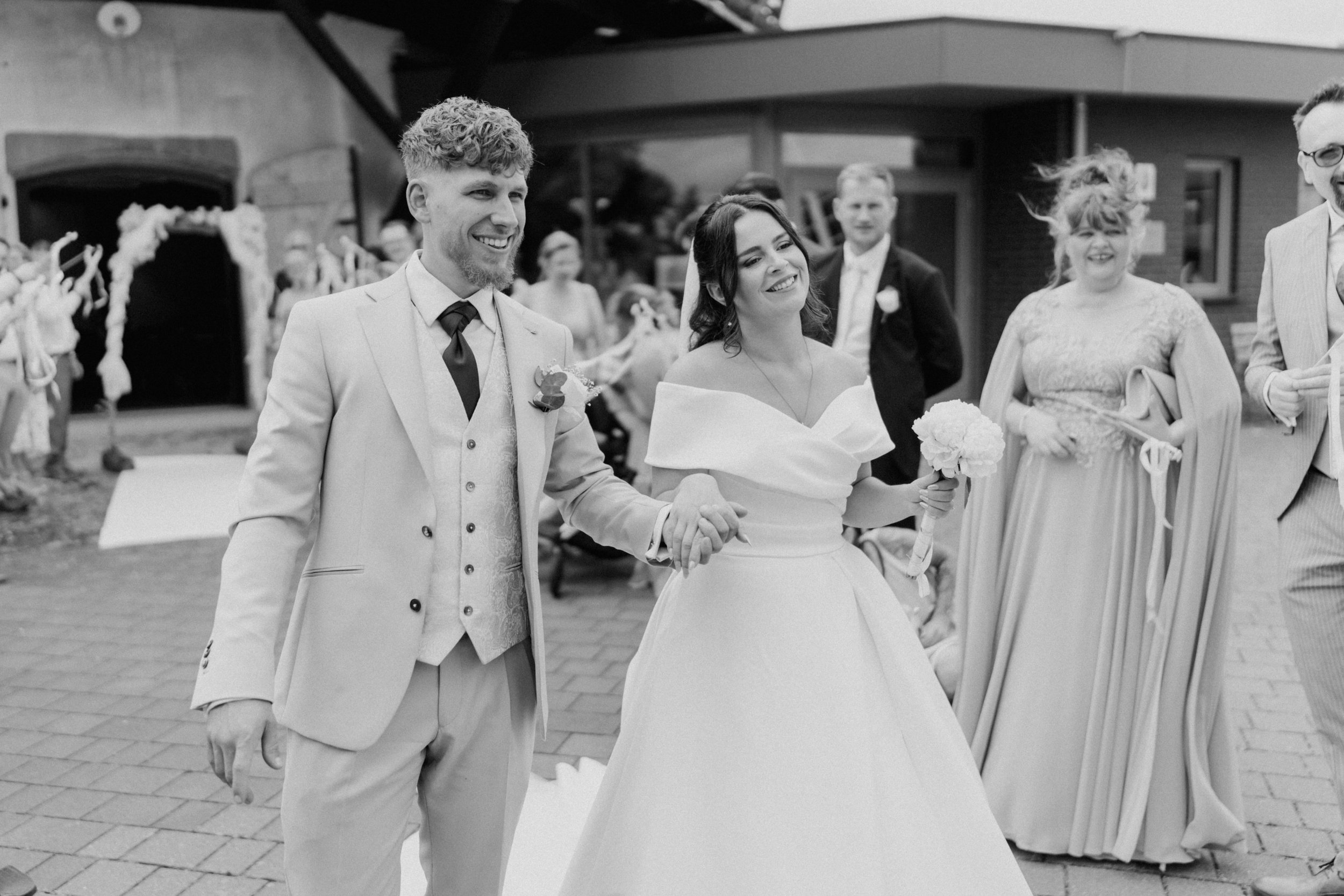 Ein Brautpaar, das an einer Hochzeit teilnimmt, umgeben von Familienmitgliedern, im Freien bei Tageslicht