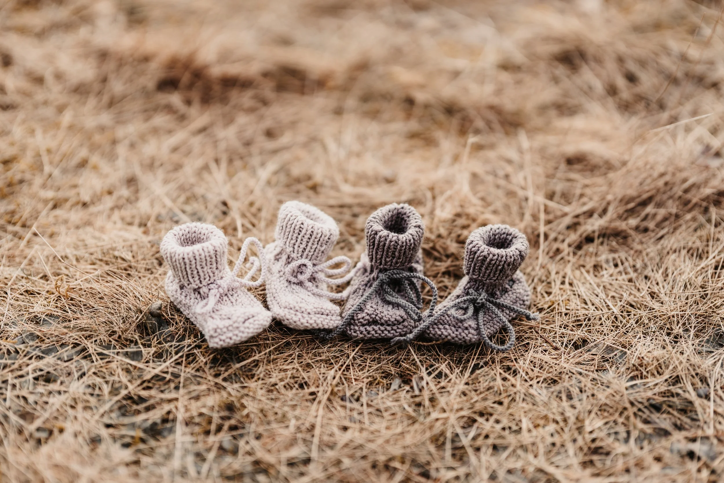 Zwei kleine gestrickte Babyschuhe auf trockenem Gras