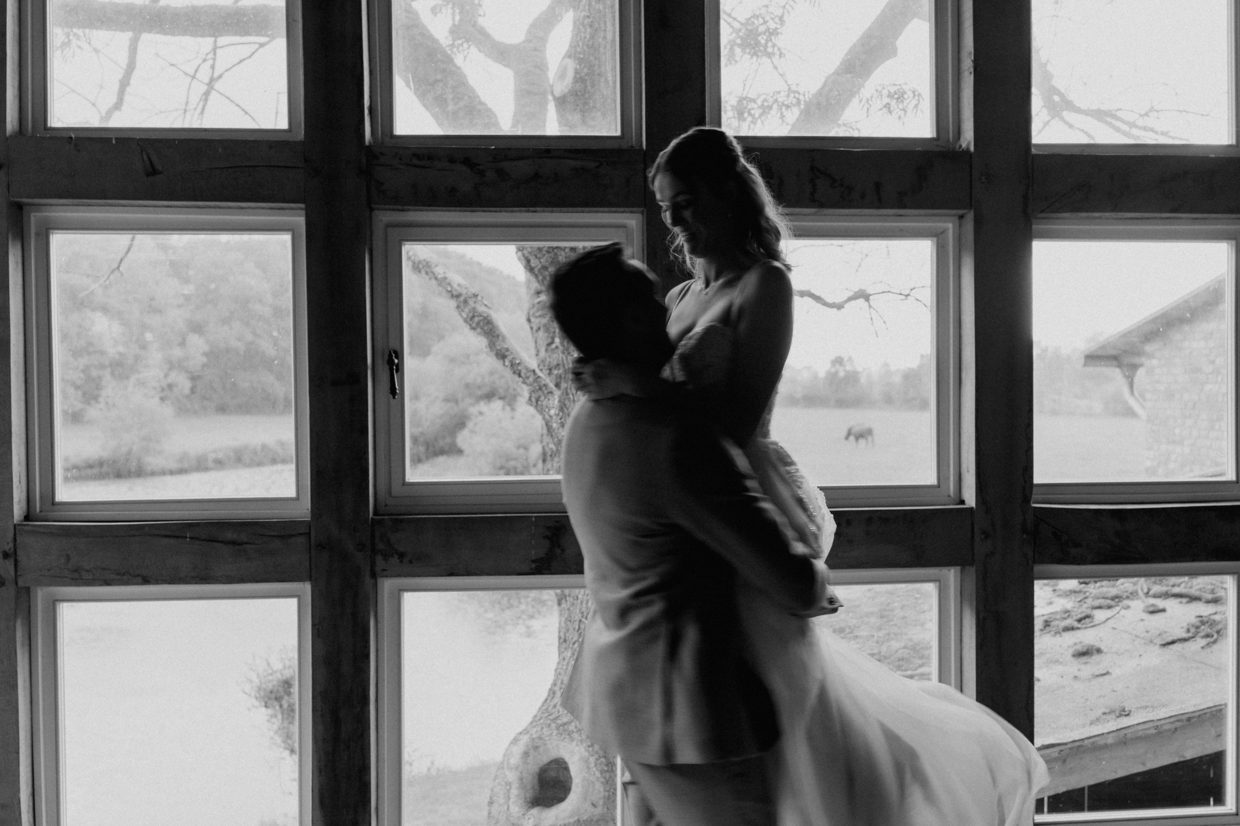 Silhouette eines Paares im Hochzeitstanz vor großen Fenstern, mit Blick auf die Natur im Hintergrund.