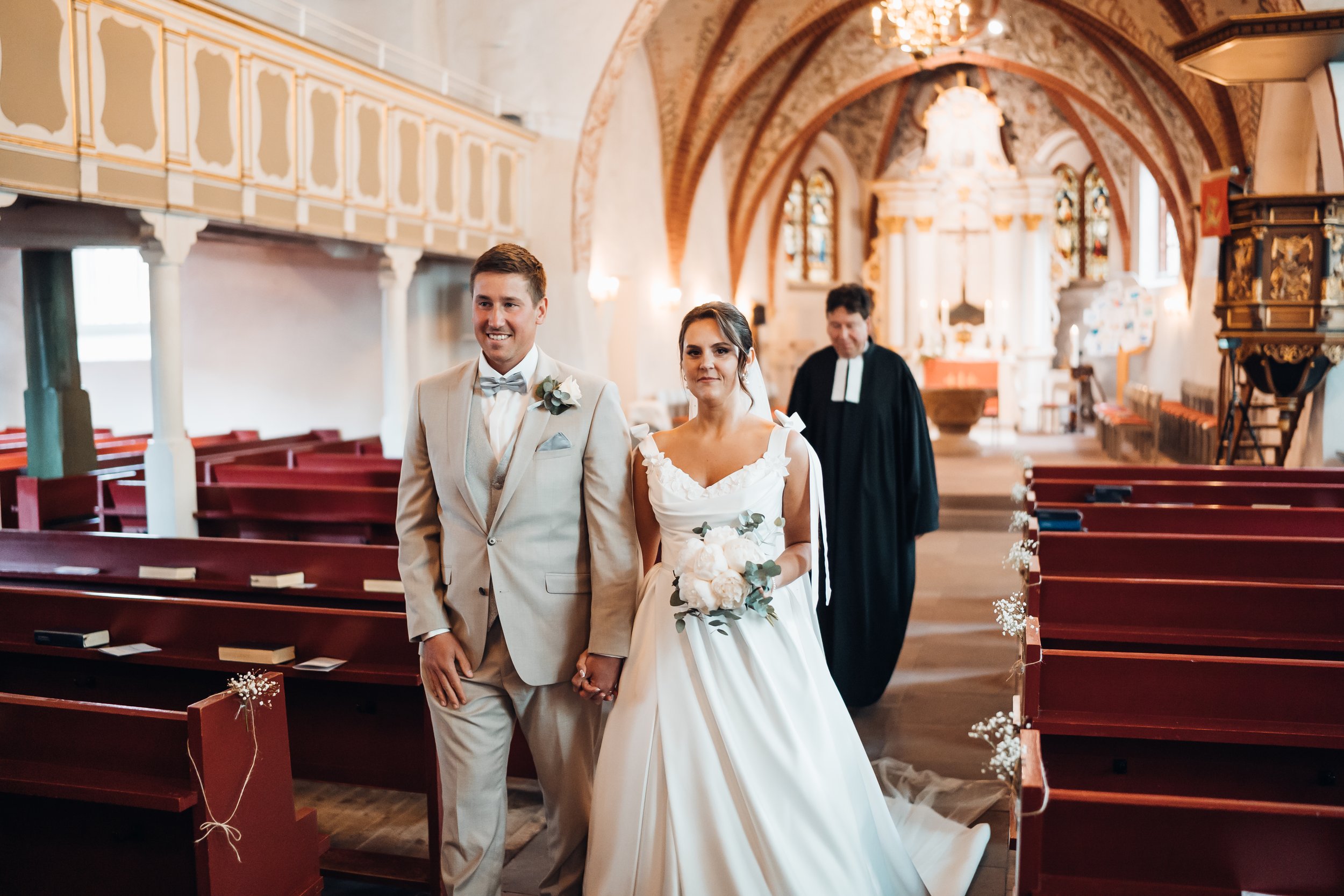 Ein frisch vermähltes Paar in einer Kirche während ihrer Hochzeitszeremonie, mit einem Priester im Hintergrund.