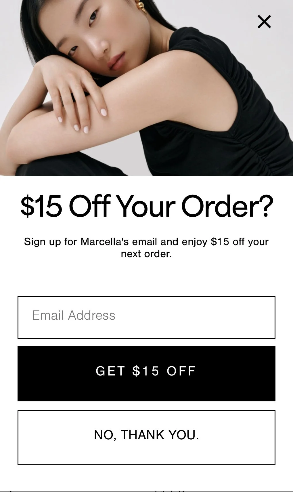 A promotional image offering $15 off an online order, featuring a young woman with long black hair and gold earrings, sitting with her arms crossed, wearing a black sleeveless top, against a plain light background.