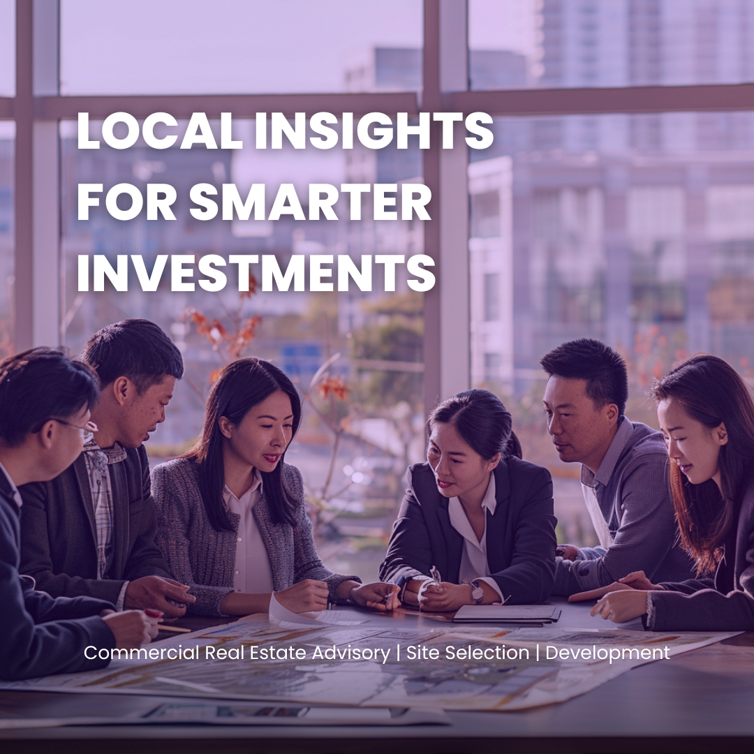 A group of six business professionals sitting around a table in a modern office, discussing documents. Large windows with cityscape views in the background.