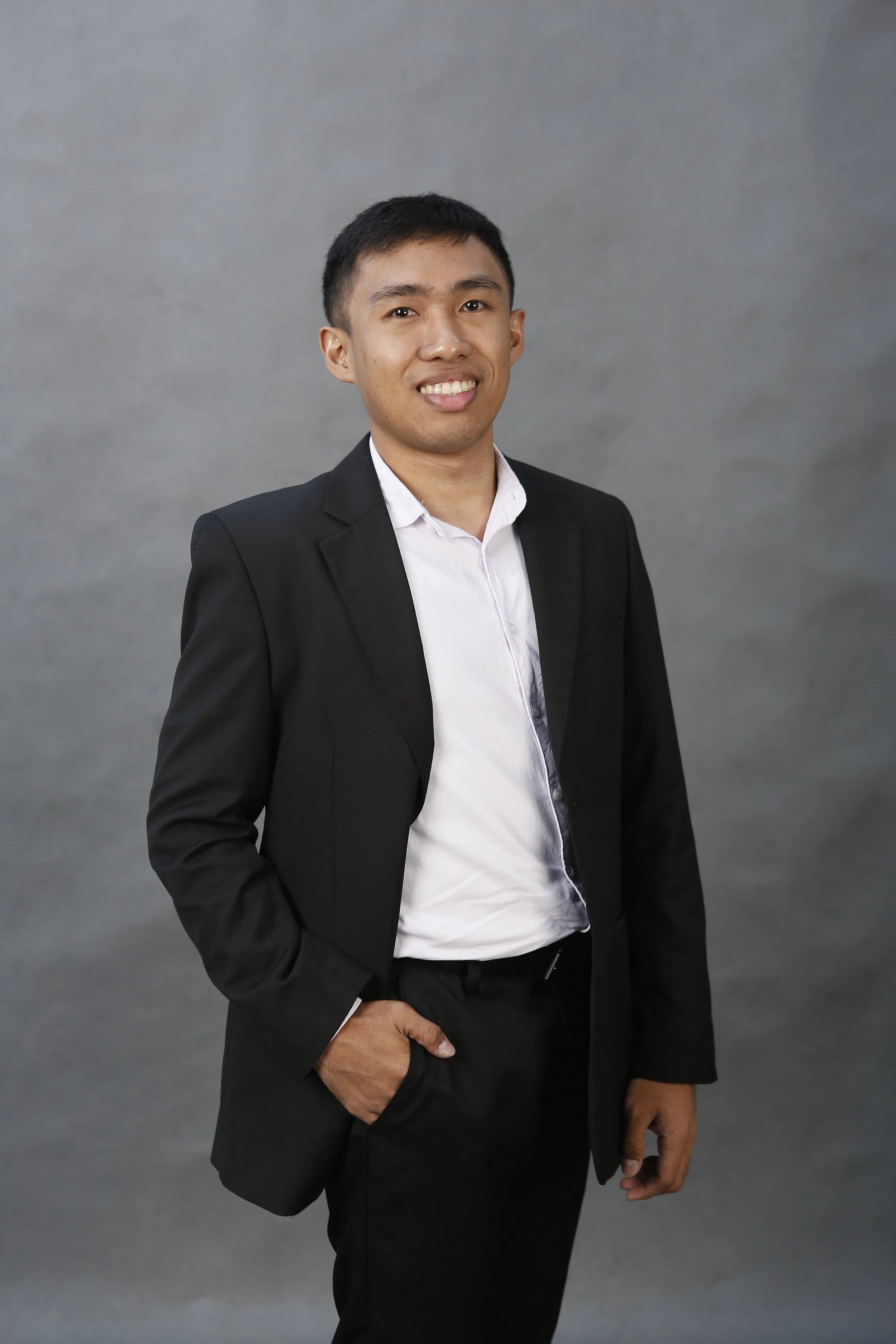 Professional portrait of a young man in a light blue shirt and dark tie, smiling, against a blue background.