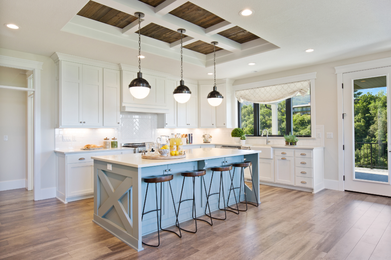 Modern kitchen with white cabinets, a large island with four barstools, pendant lighting, a window with a Roman shade, and a door leading outside.