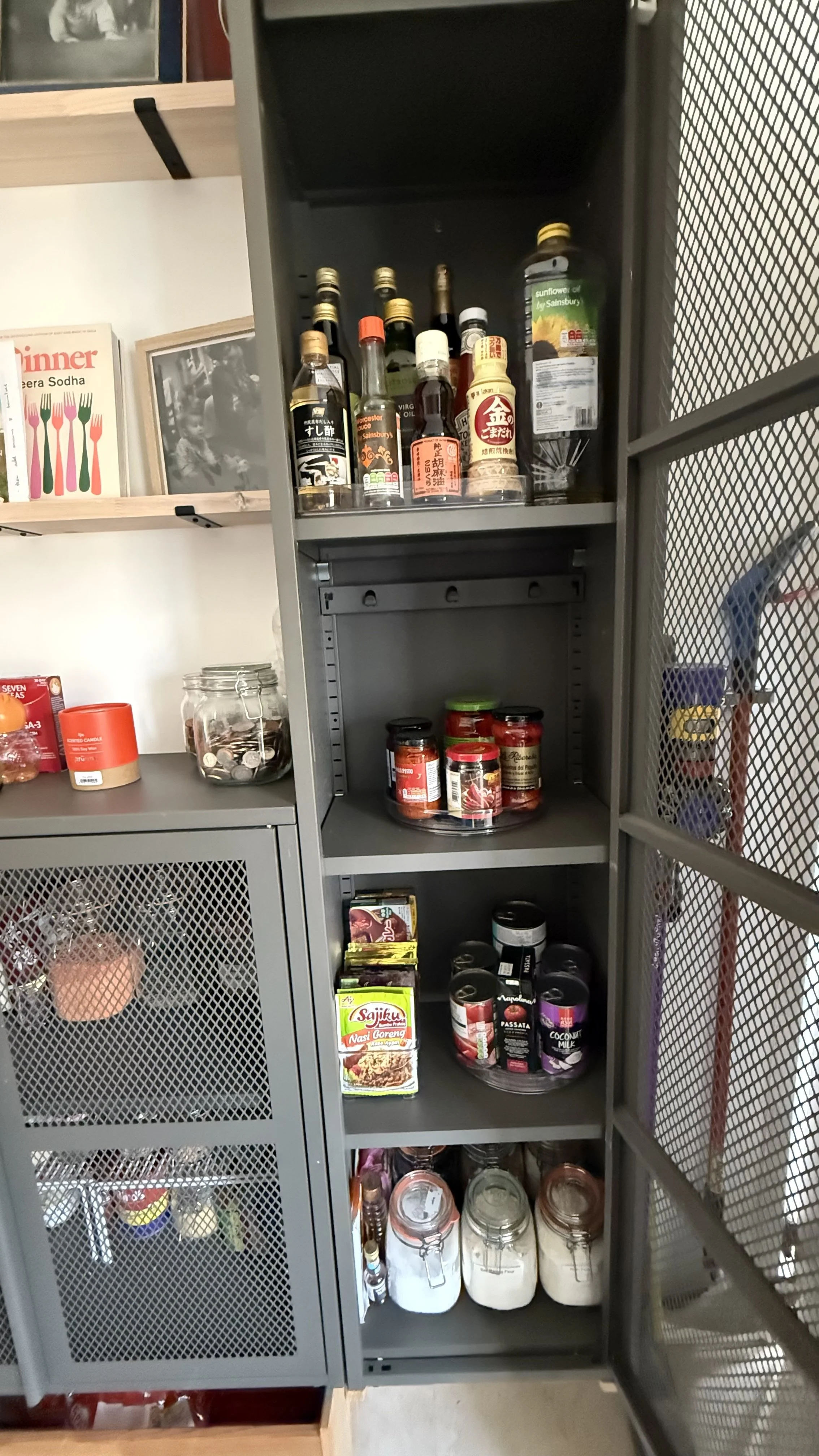A kitchen shelf with various bottles of sauces and condiments on the top shelf, jars of spices and sauces on the middle shelf, and containers of rice and other dry goods on the bottom shelf, all in a modern kitchen setting.