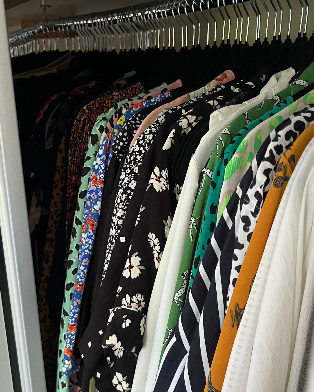 Clothing rack with a variety of colorful patterned shirts and dresses hanging on it.