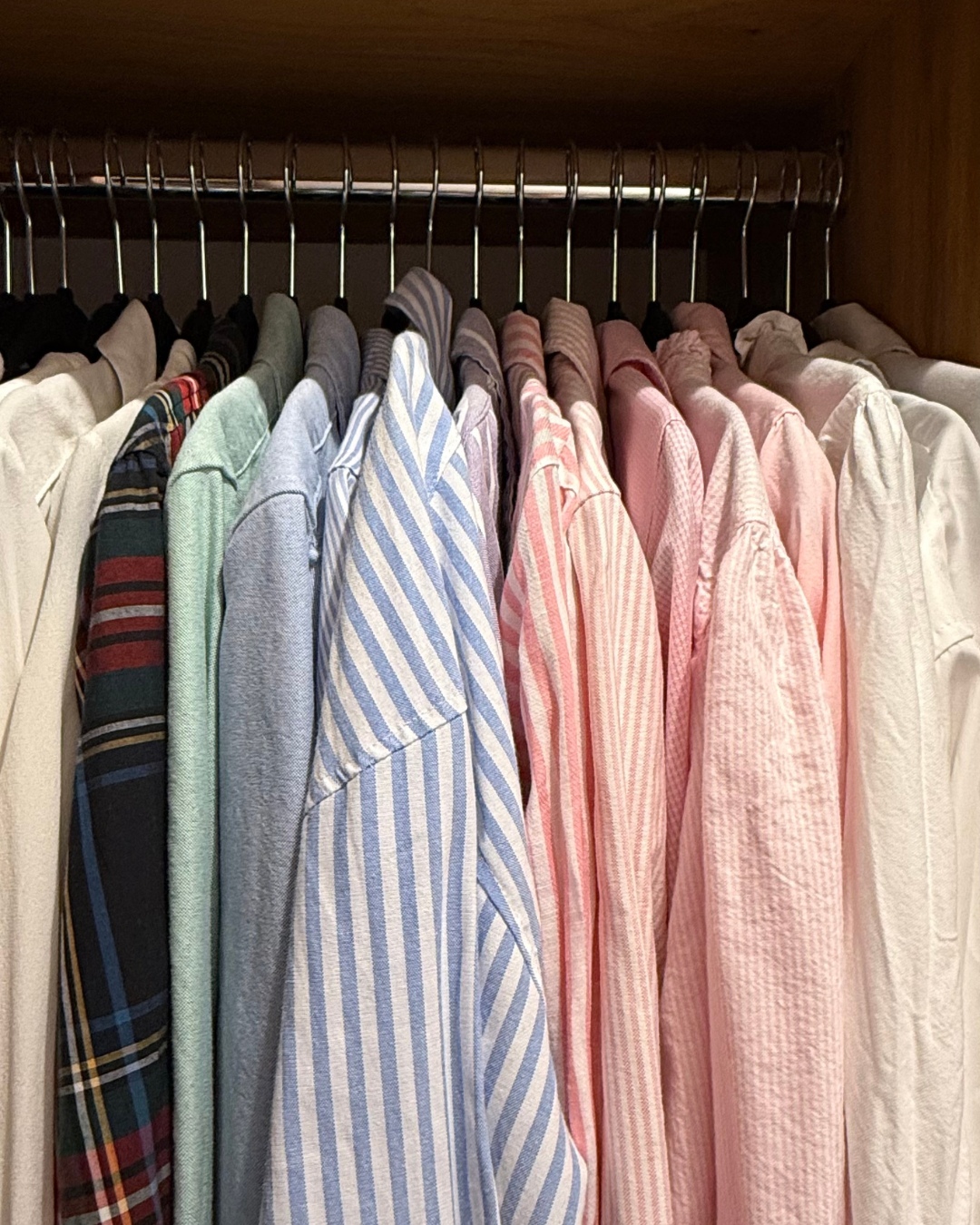 A wardrobe shelf with a row of collared shirts in various colours and patterns, hanging on slimline hangers.