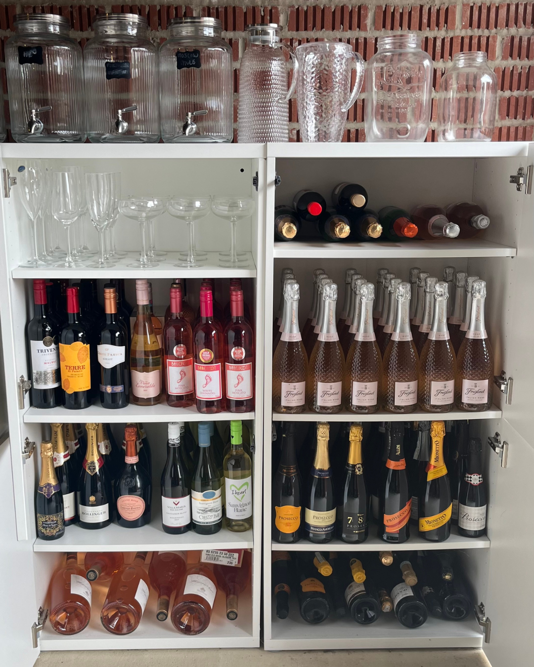 Cabinet filled with various bottles of wine, champagne, and glassware, organized by type and color.